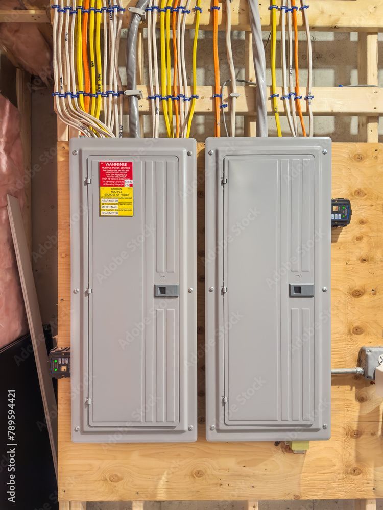 Two gray electrical panels mounted on wooden studs with colored wires above.