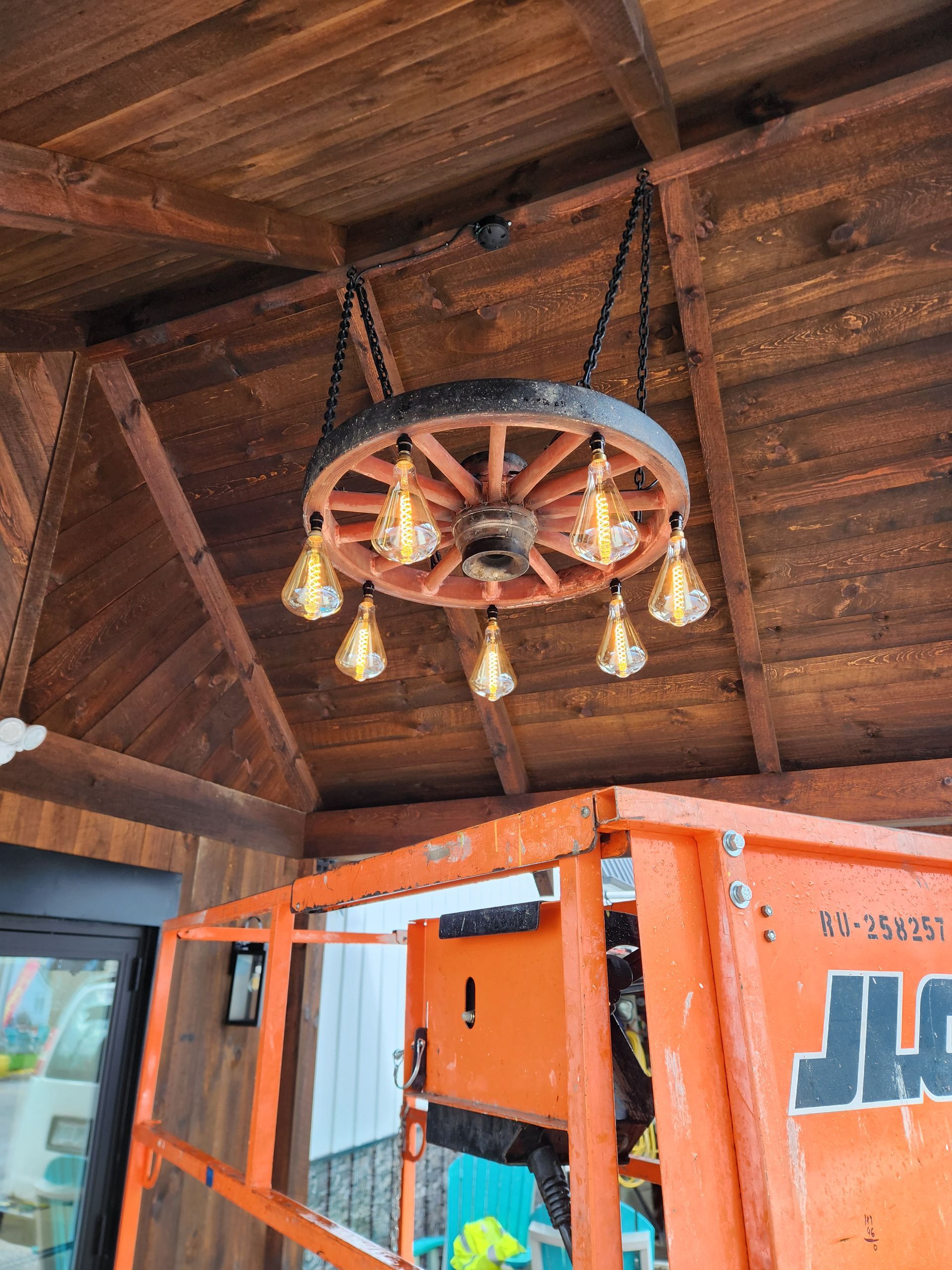 Wooden wagon wheel chandelier with Edison bulbs hanging from a wood ceiling, with a lift below.