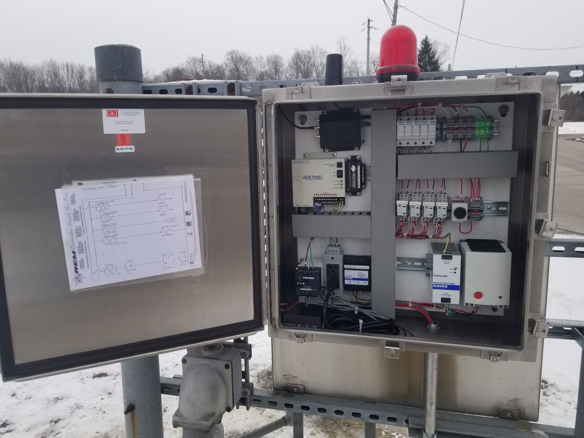 Open control panel box on a snowy day. Stainless steel, components visible inside. Red light on top.