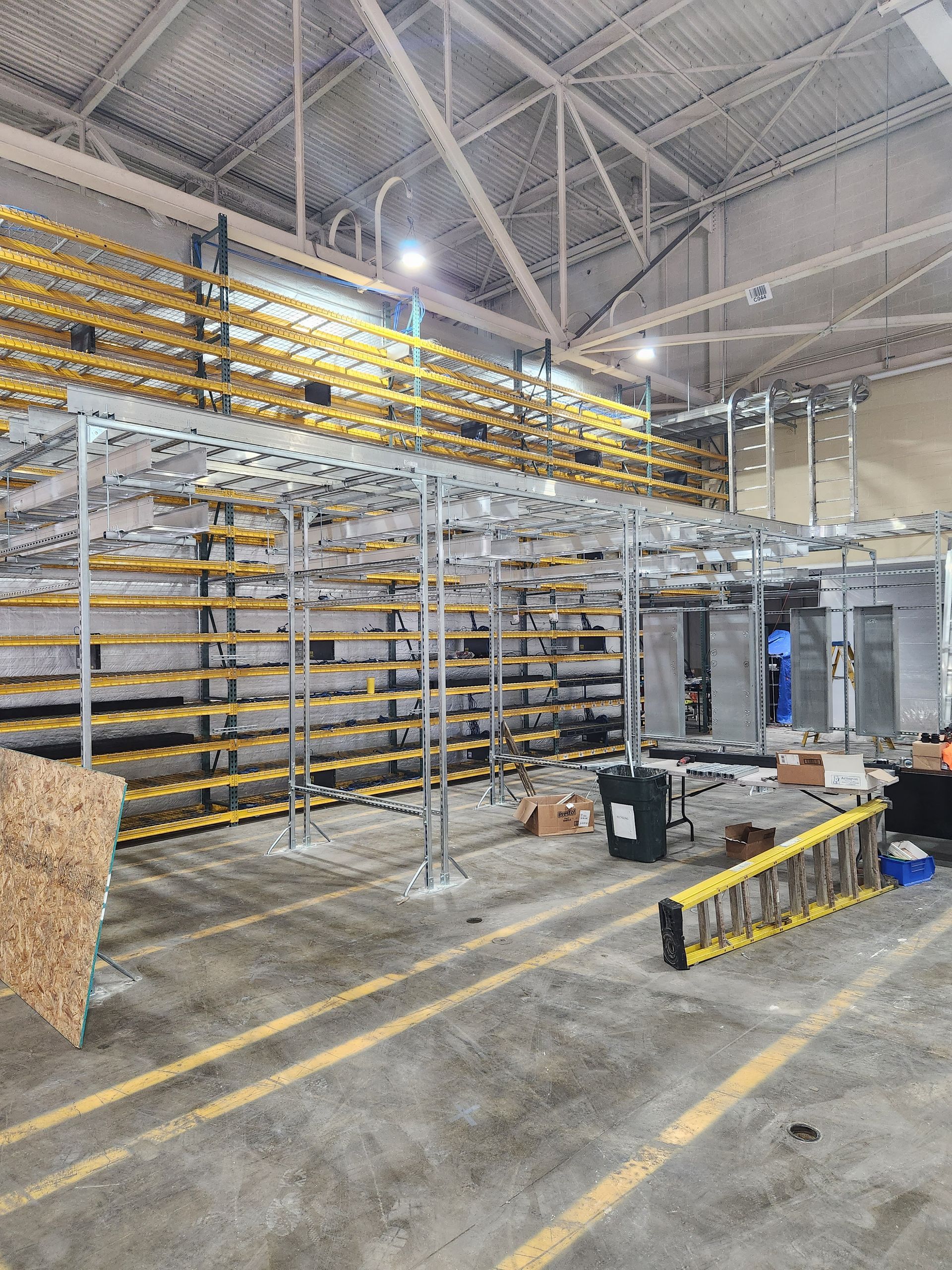 Interior of a warehouse with metal shelving units; some sections are yellow. Concrete floor with painted yellow lines.