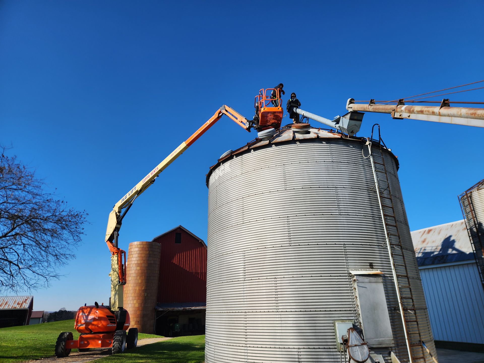Workers in a lift repair a grain silo on a farm, sunny day.