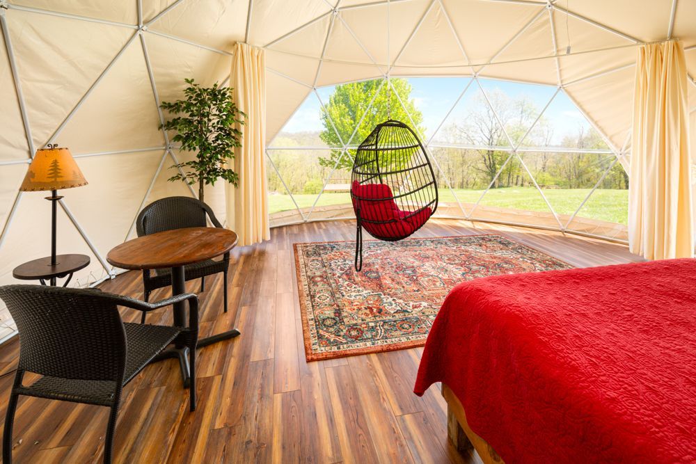 A bedroom with a bed , chairs , a table and a hanging chair.