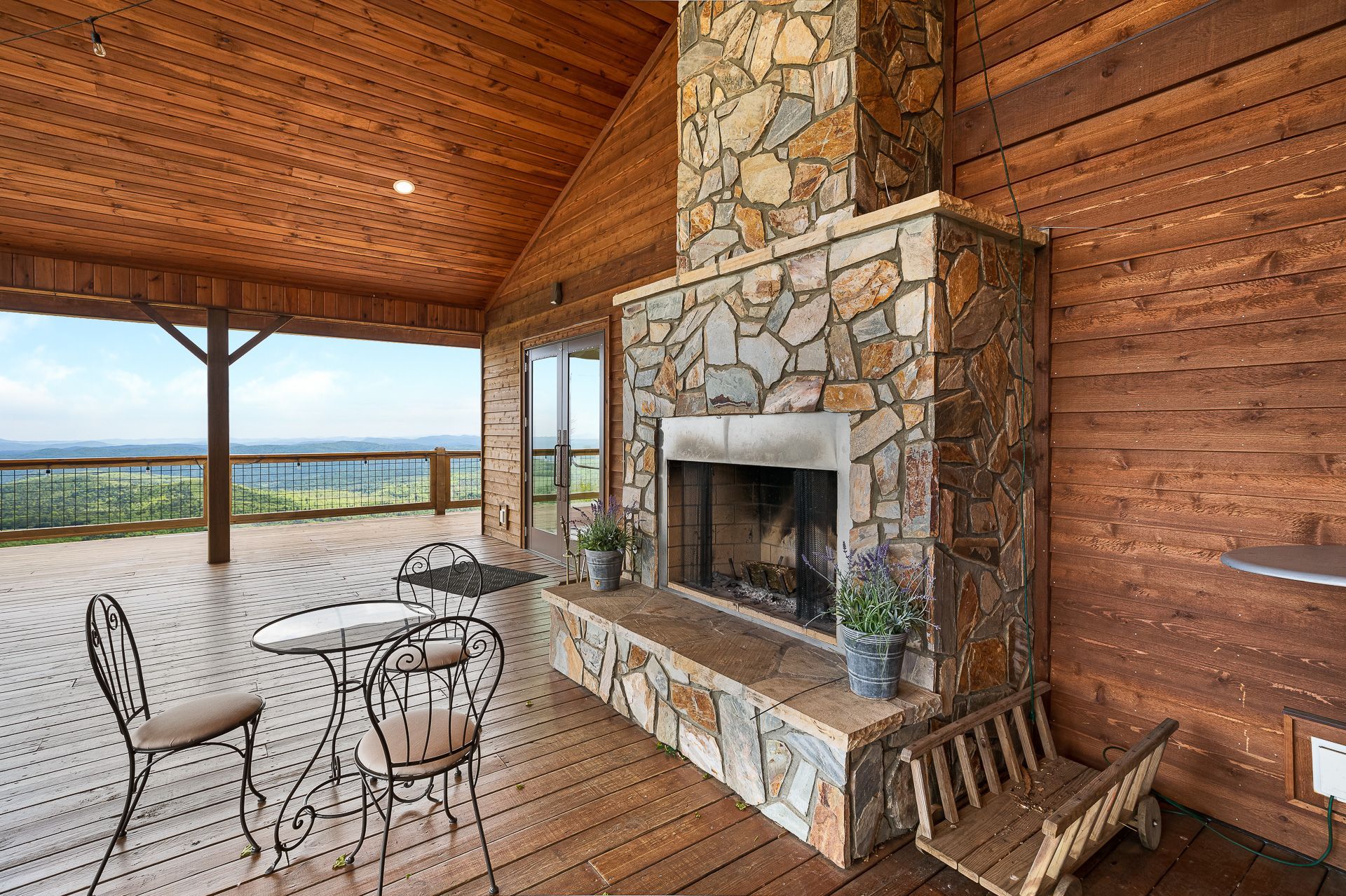 A wooden deck with a stone fireplace and a table and chairs.