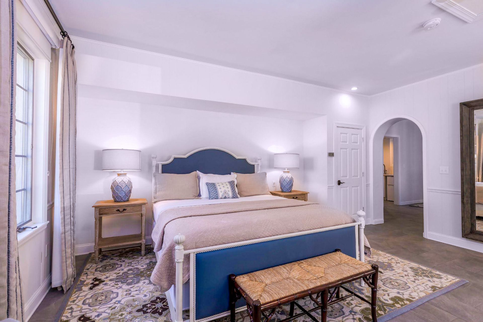 A bedroom with a king size bed , nightstands , lamps , and a bench.