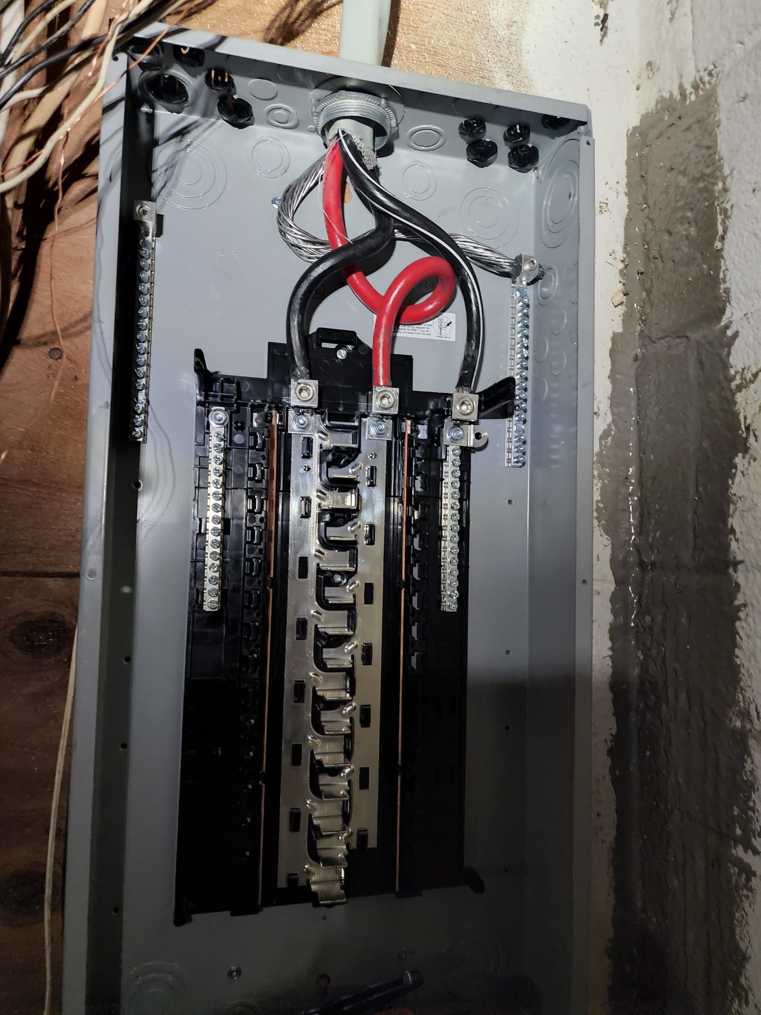 An open residential electrical breaker panel with two thick black and red service wires connected to the central lugs.
