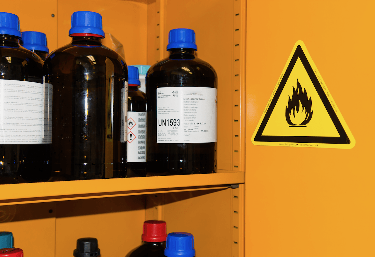 A yellow cabinet with bottles of chemicals and a warning sign