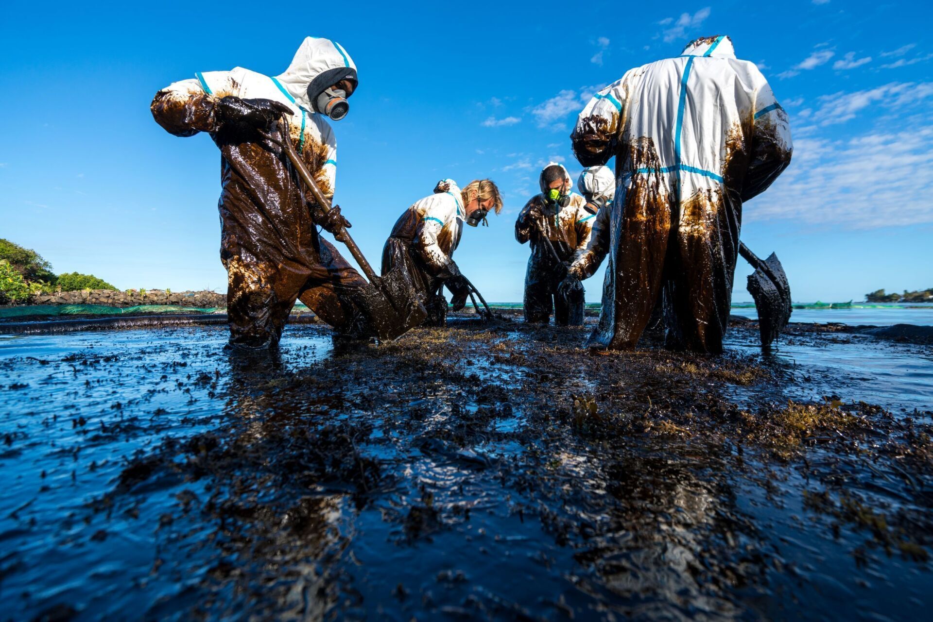 A group of people in protective suits are working in a muddy area.