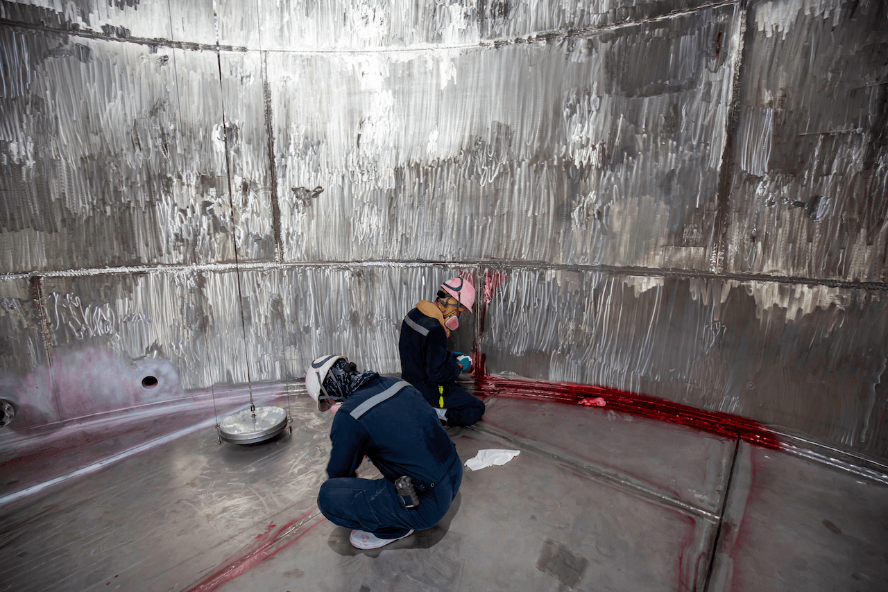 A man is kneeling down in a large metal tank.