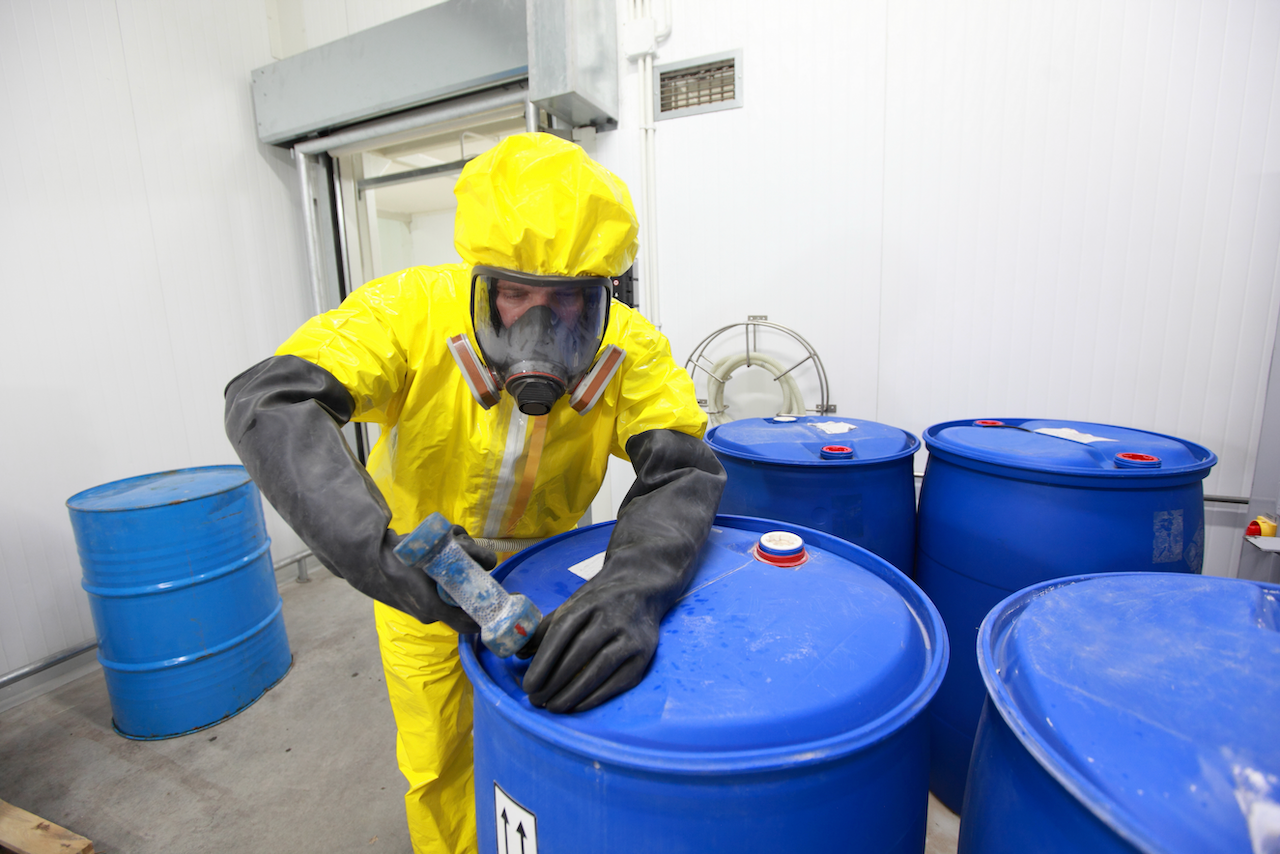 A man in a yellow protective suit is working on a blue barrel