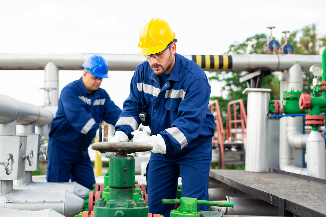 Two men are working on a valve in an oil refinery.