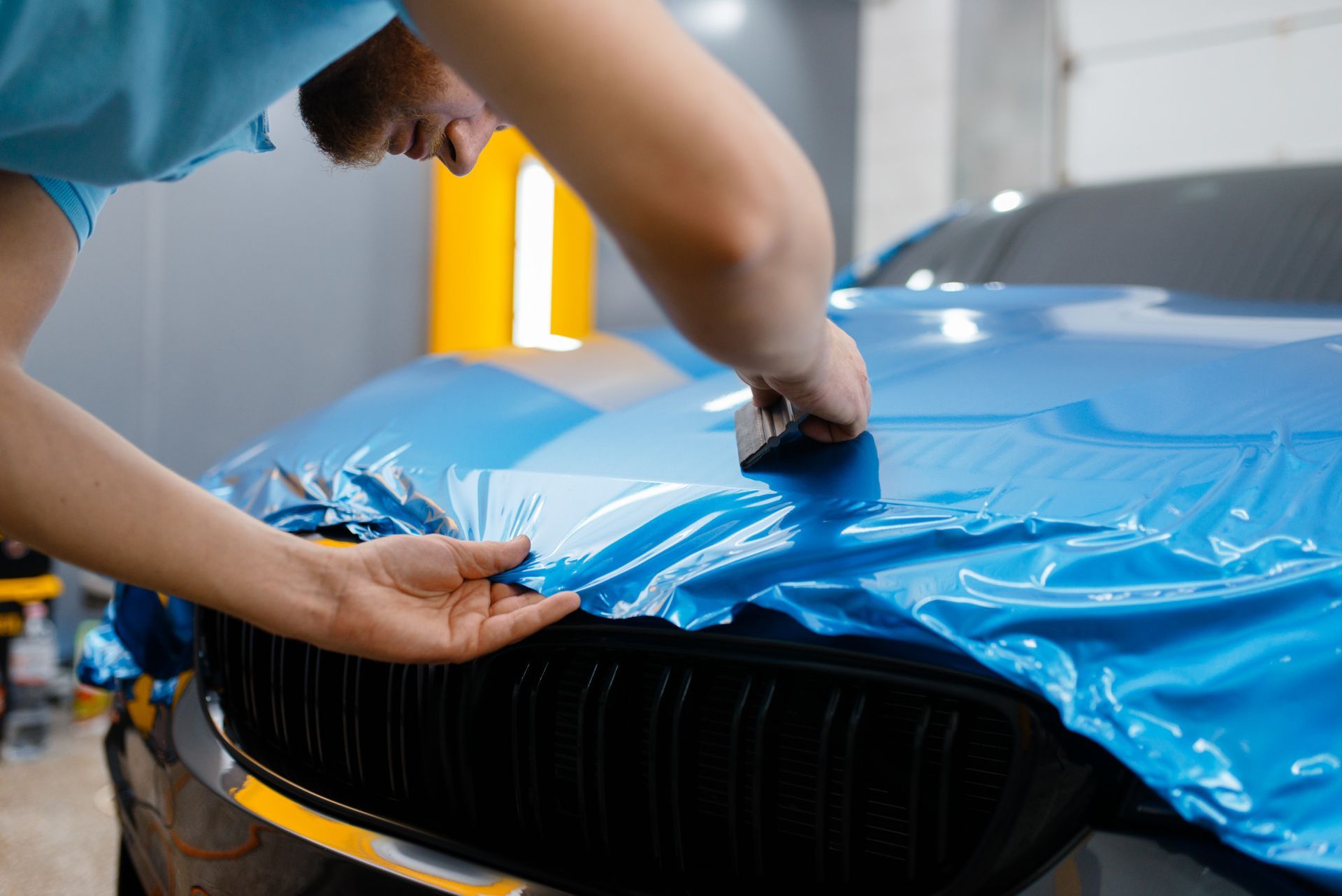 A man is wrapping a blue car with blue plastic wrap.