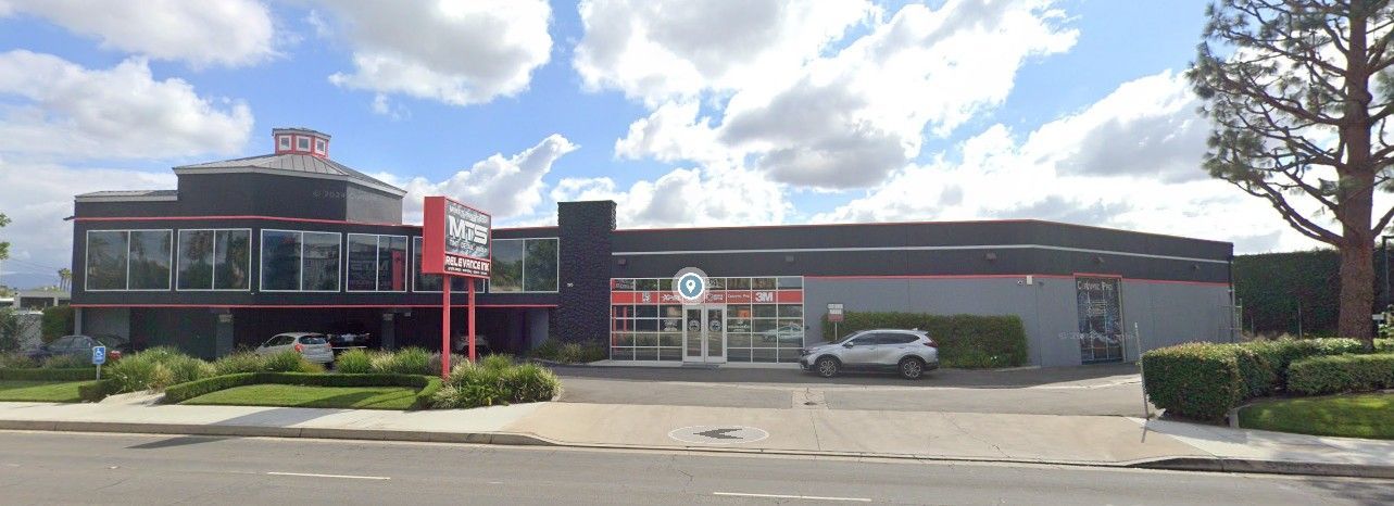 Exterior of a business with red signage and a dark facade; trees and cloudy blue sky in the background.