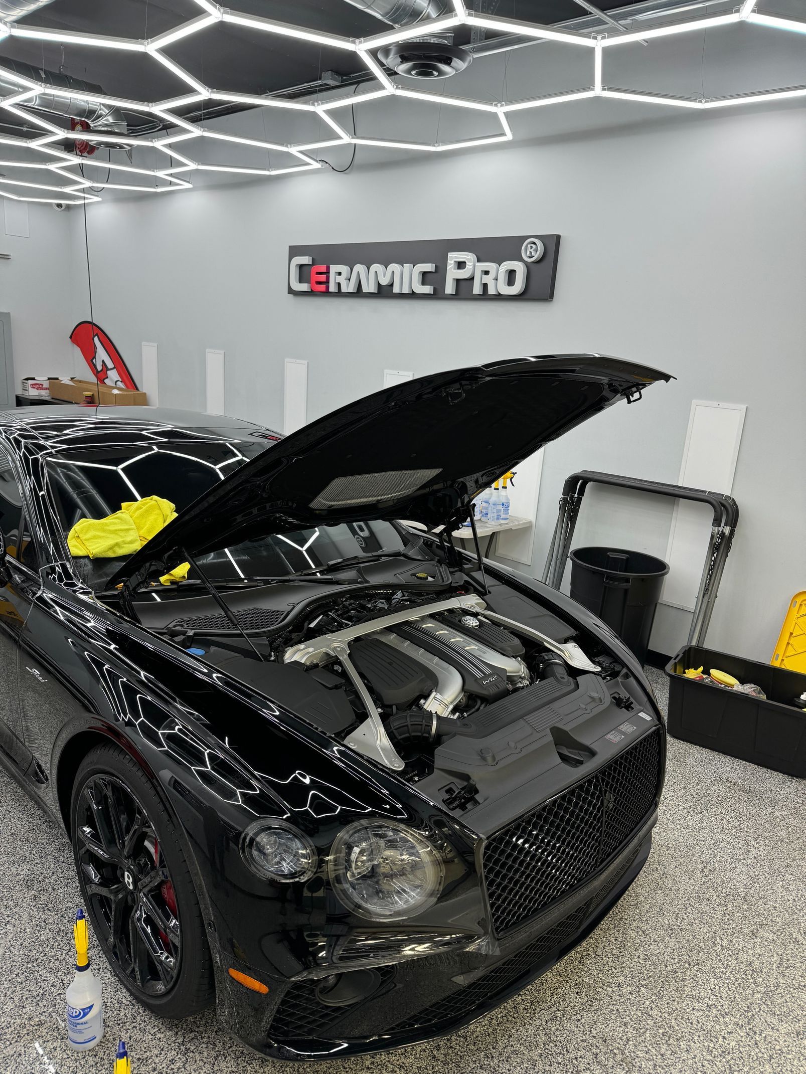 A black car with the hood up is sitting in a garage.