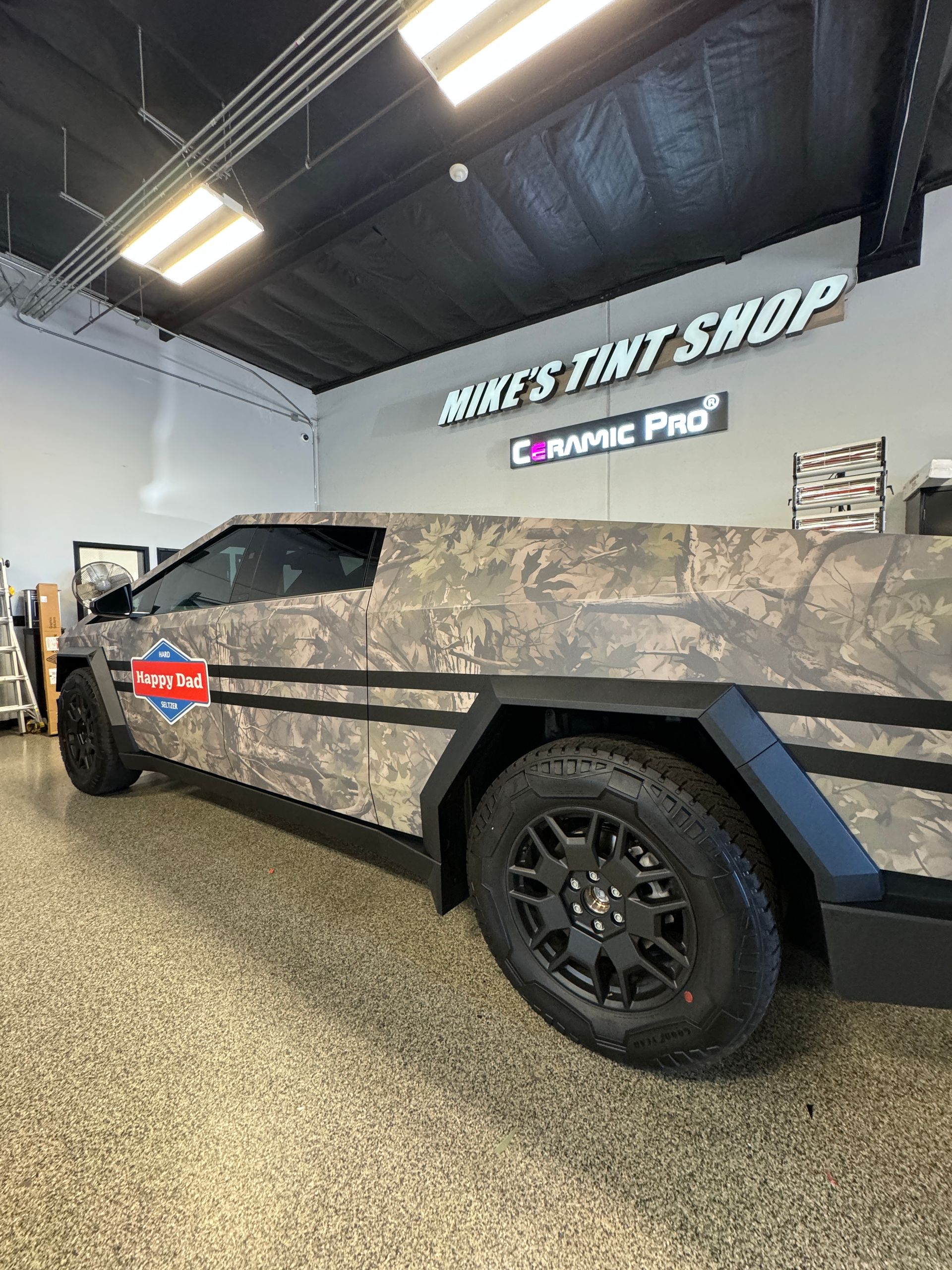 A car wrapped in camouflage is parked in a garage.