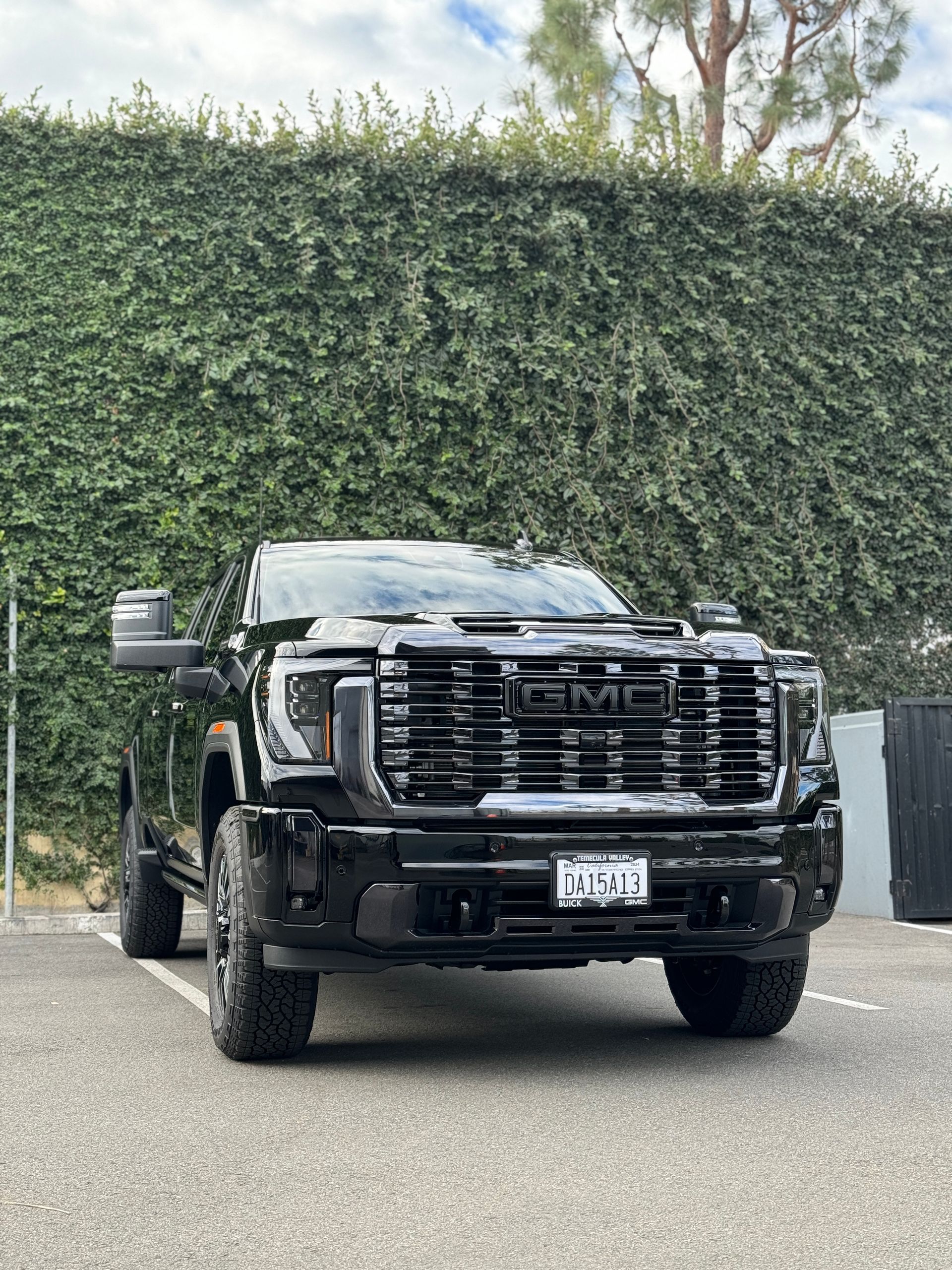 A black truck is parked in a parking lot in front of a hedge.