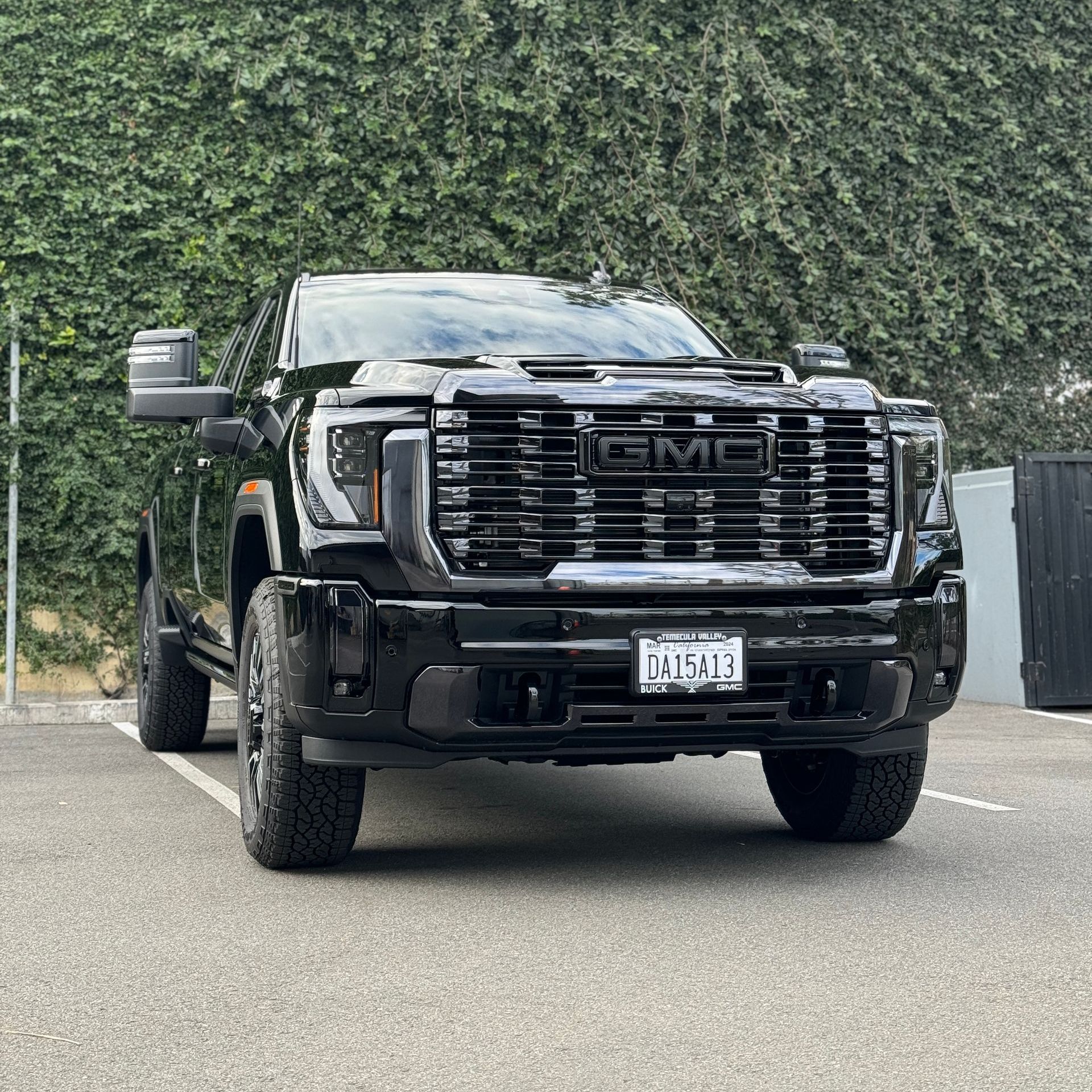 A black truck is parked in a parking lot with trees in the background.