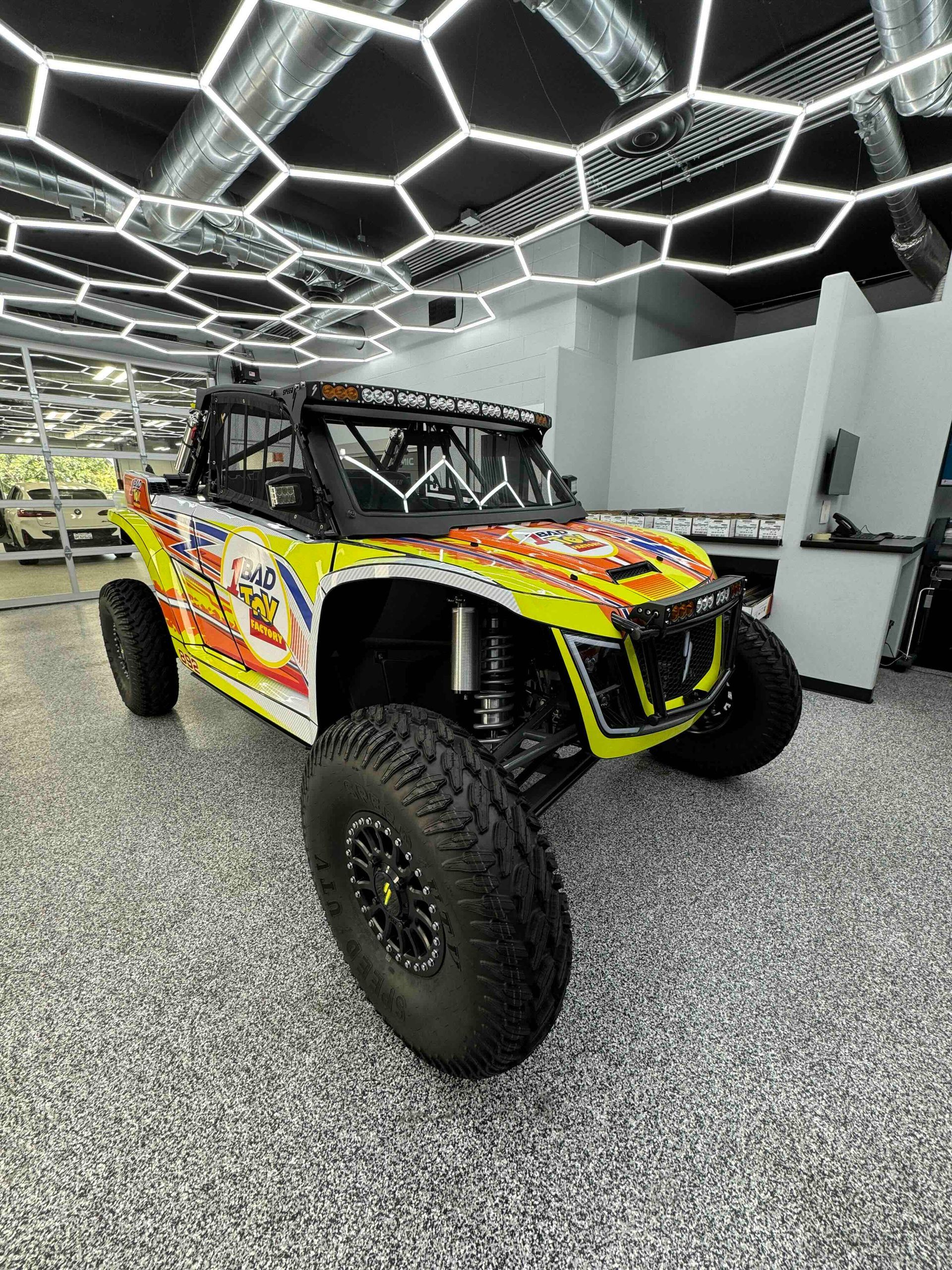 Yellow and white off-road vehicle with large tires parked indoors under honeycomb ceiling lights.