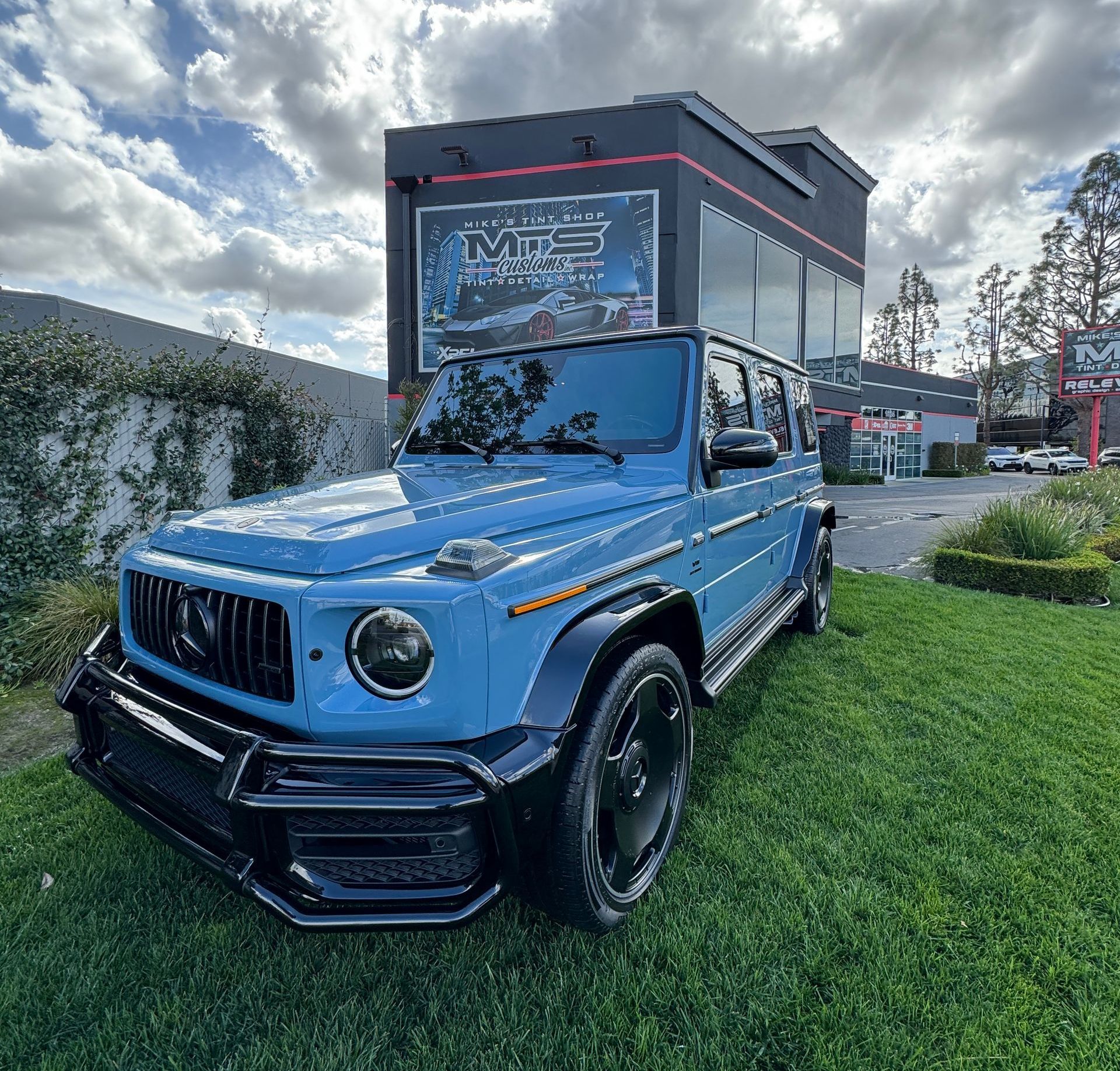 A blue mercedes benz g63 is parked in front of a building.