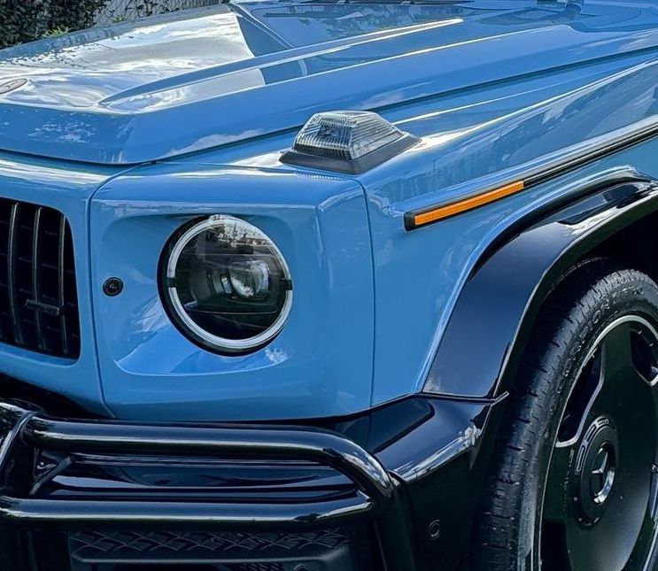 Blue Mercedes-Benz G-Class SUV, front view, black trim, round headlight, turn signal, close-up.