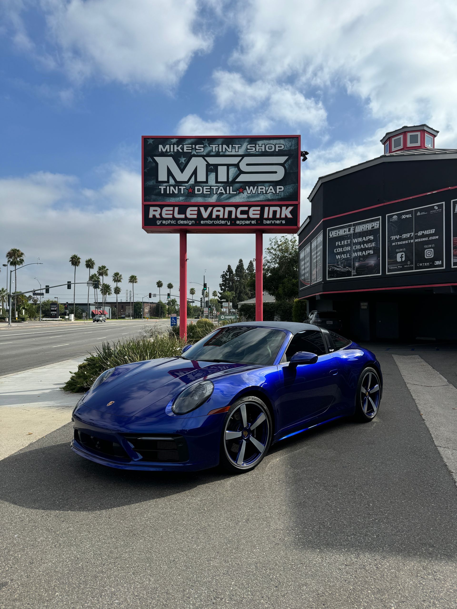 Black Tesla with opened doors, front bumper peeling, in a bright garage.