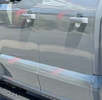Silver truck door with chrome handles, reflecting surrounding objects.