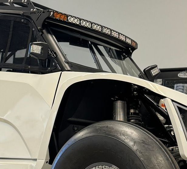 White off-road vehicle with black accents and large sand tires. Bright LED light bar on top.