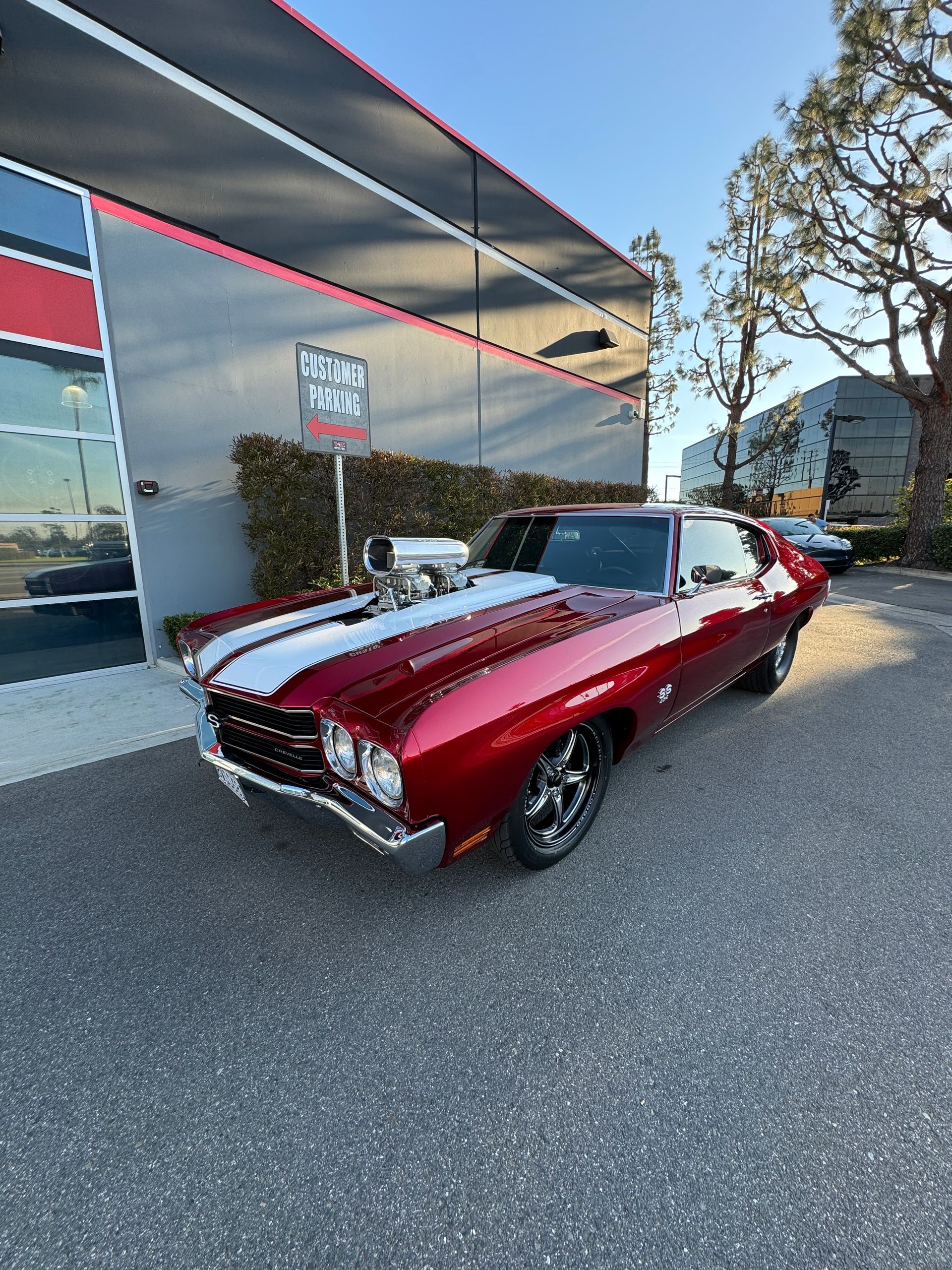 A red muscle car is parked in front of a building.