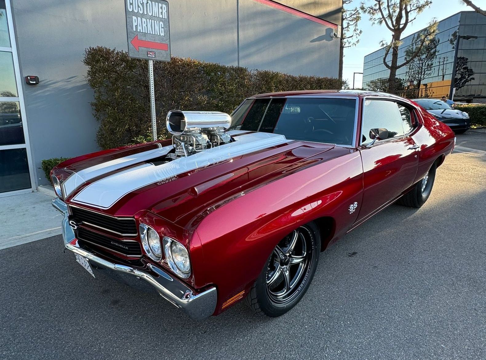A red muscle car is parked in front of a building.