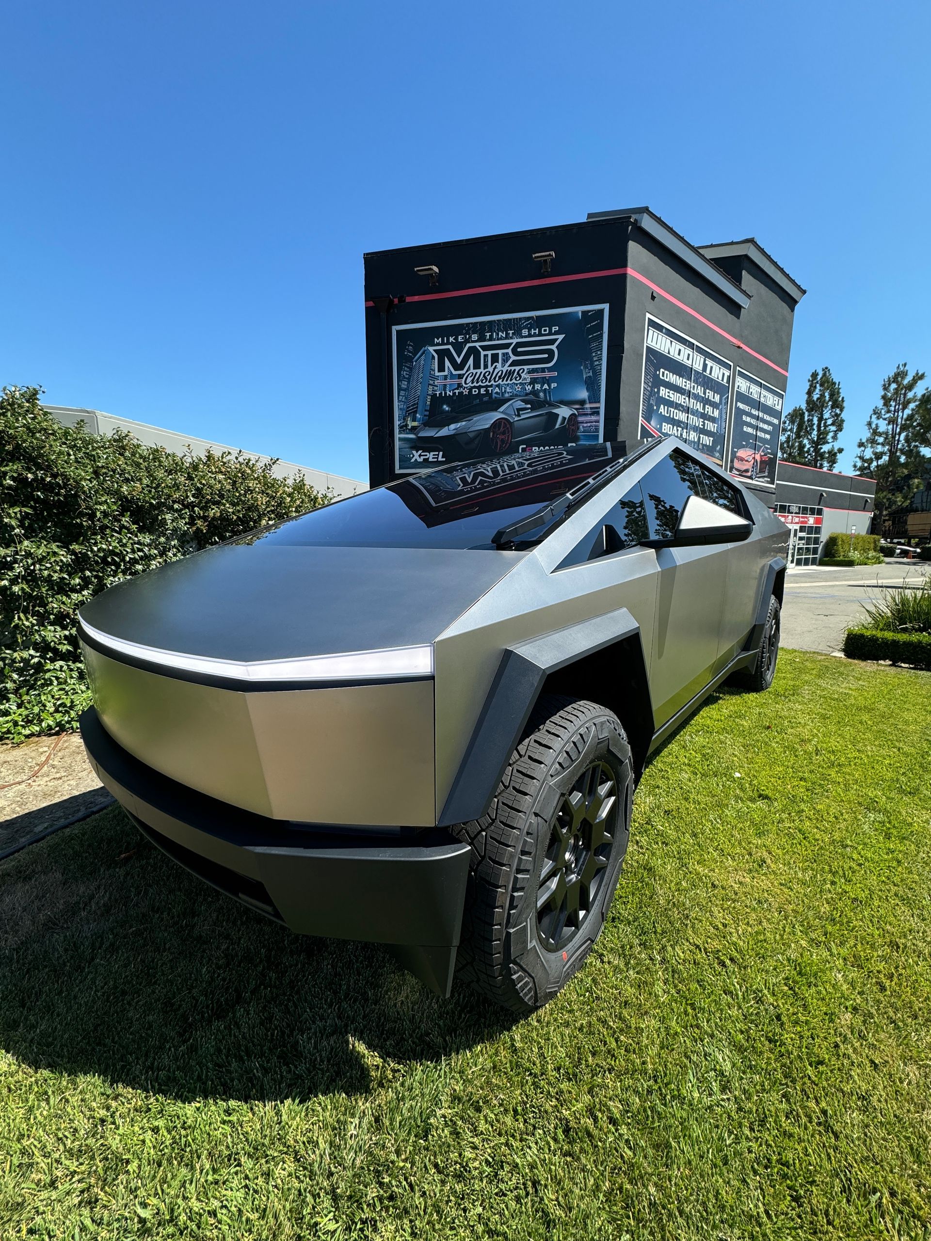 A silver tesla cybertruck is parked in the grass in front of a building.