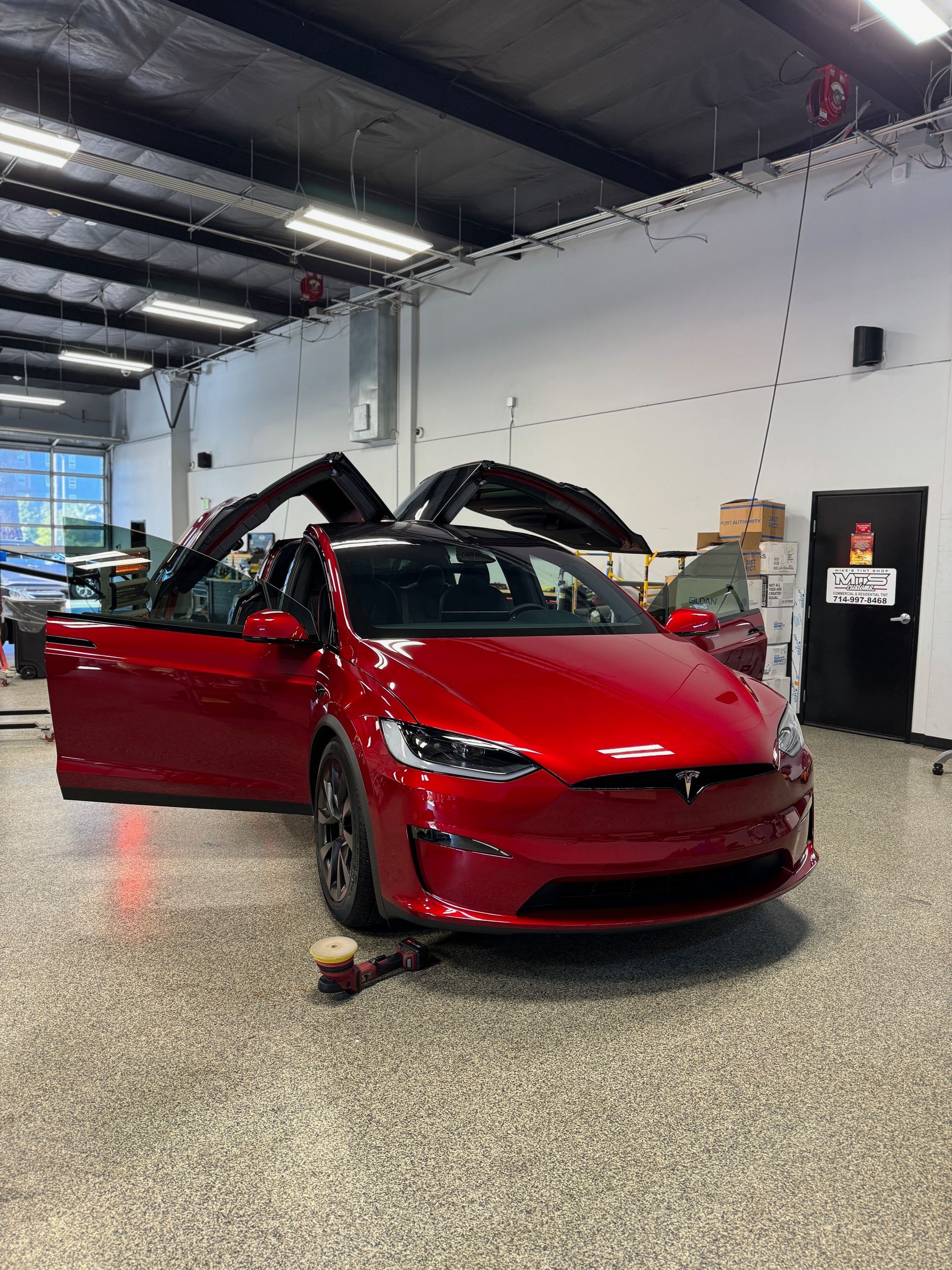 A red tesla model x is parked in a garage with its doors open.