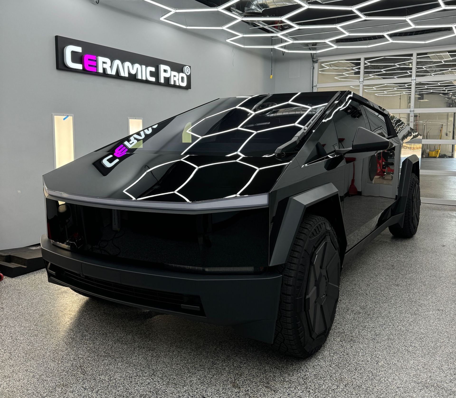 A black car is parked in a garage under a sign that says ceramic pro.