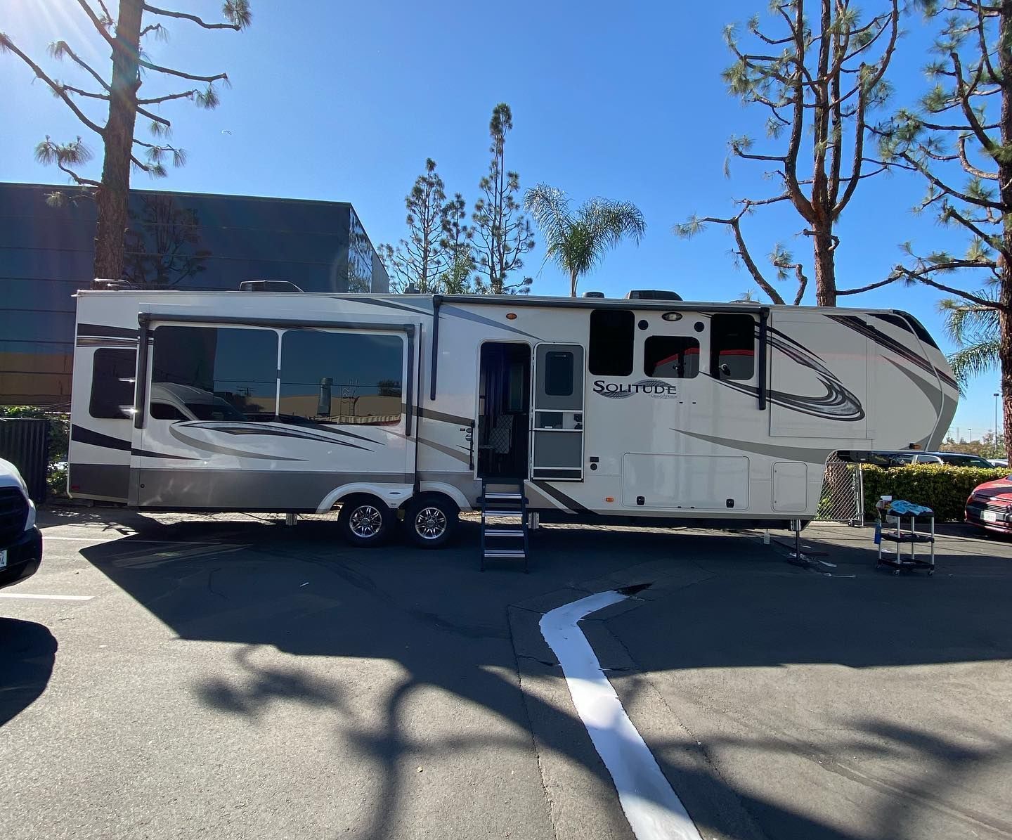 Large, white RV parked in a paved lot; a few trees are visible.
