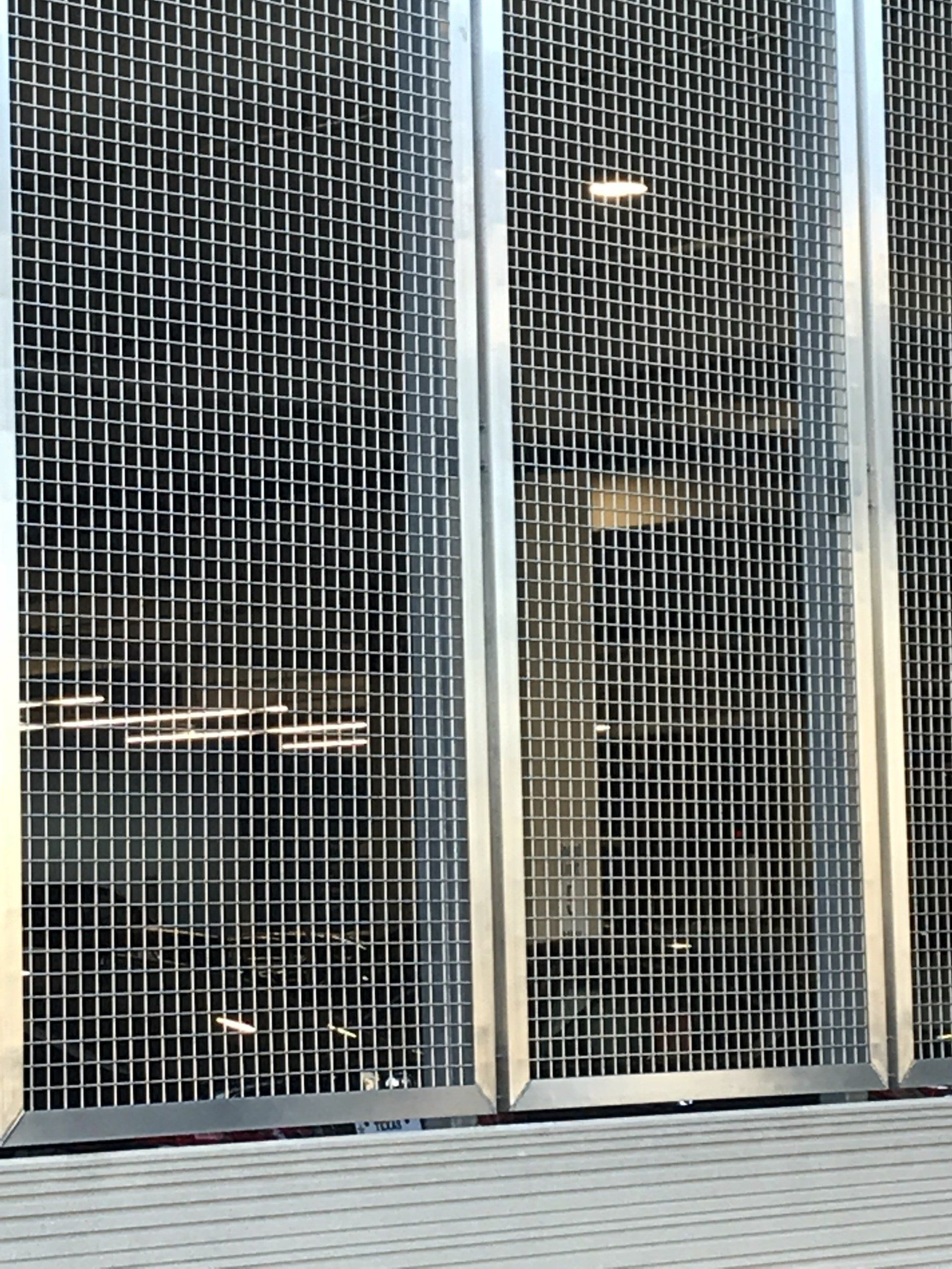 A close up of a metal fence with a window in the background.
