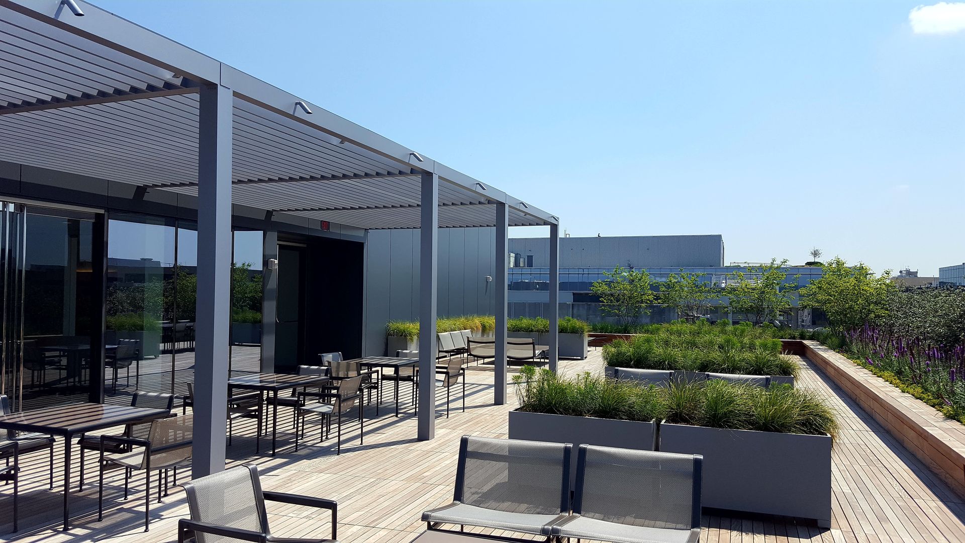 A rooftop deck with a pergola , chairs , tables and planters.