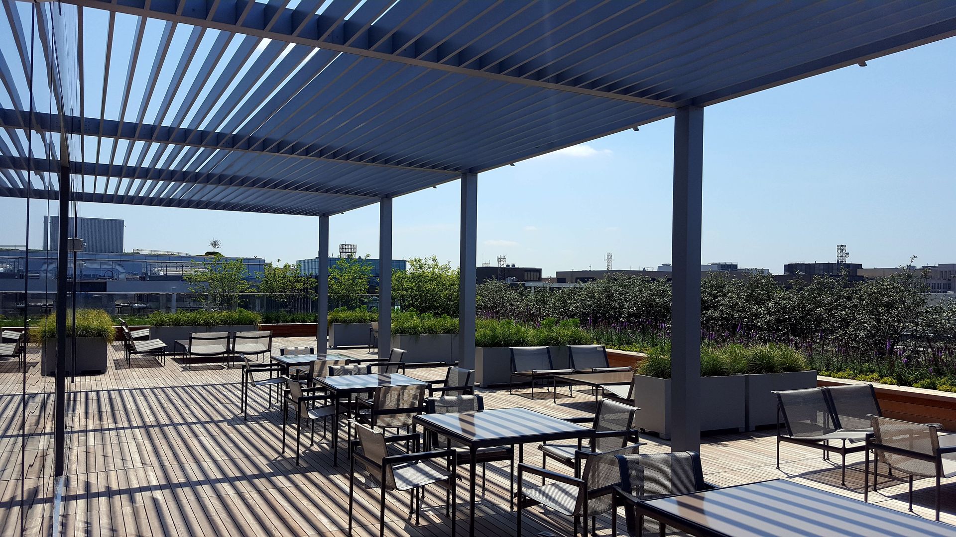 A patio with tables and chairs under a pergola on a sunny day.