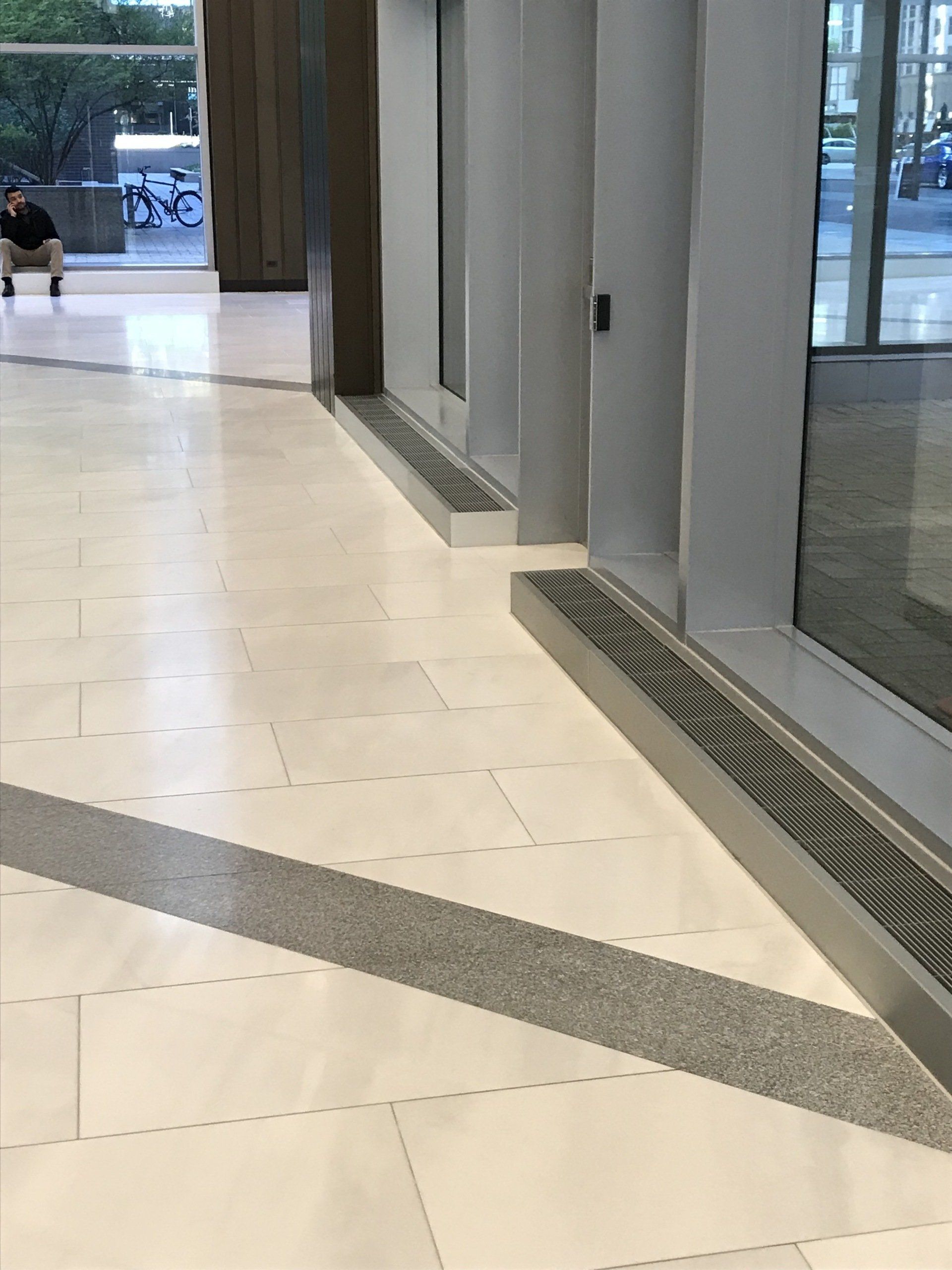 A man is sitting on a bench in a hallway next to a window.