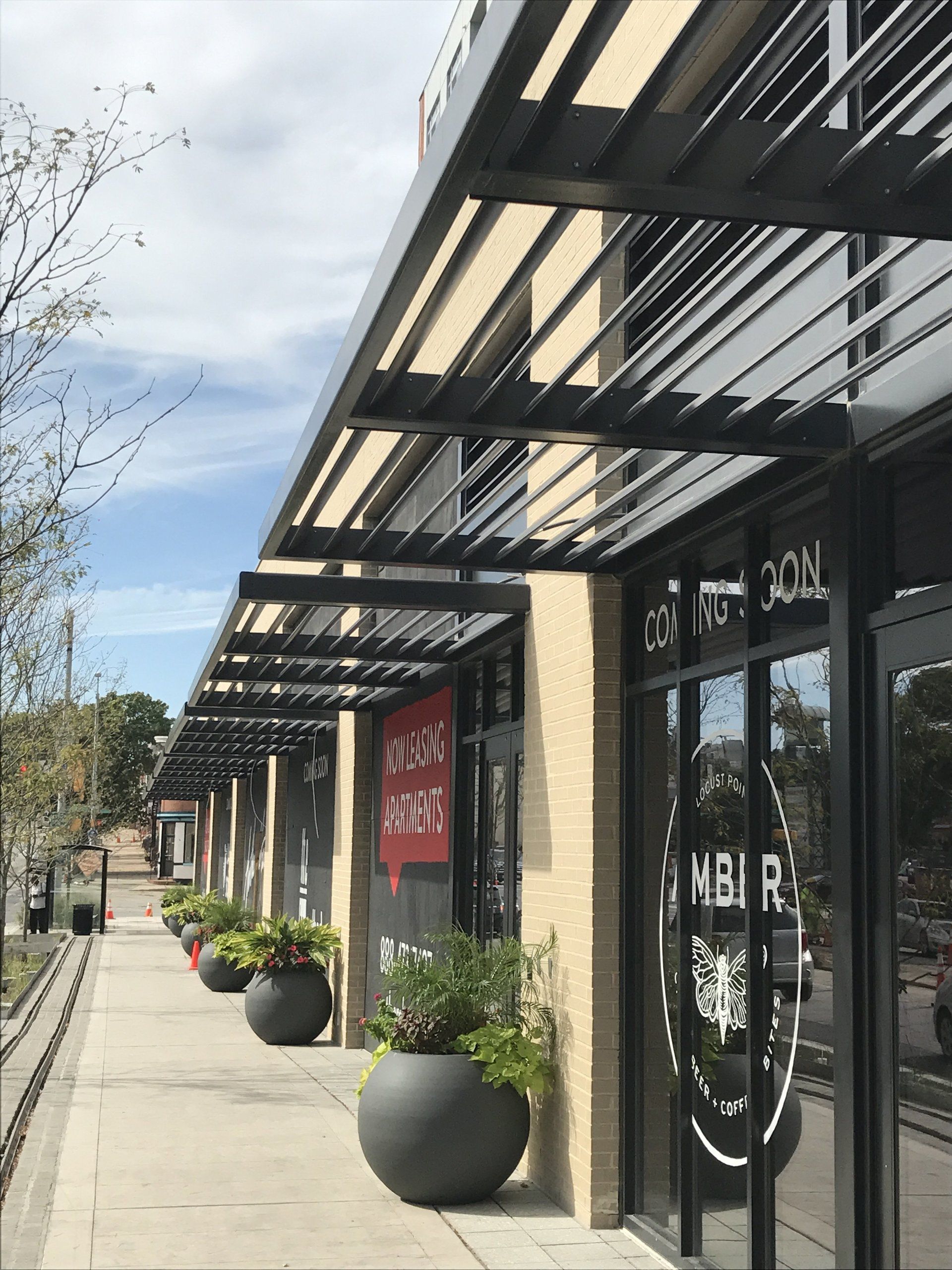 A row of potted plants on a sidewalk in front of a building that says mbi r.