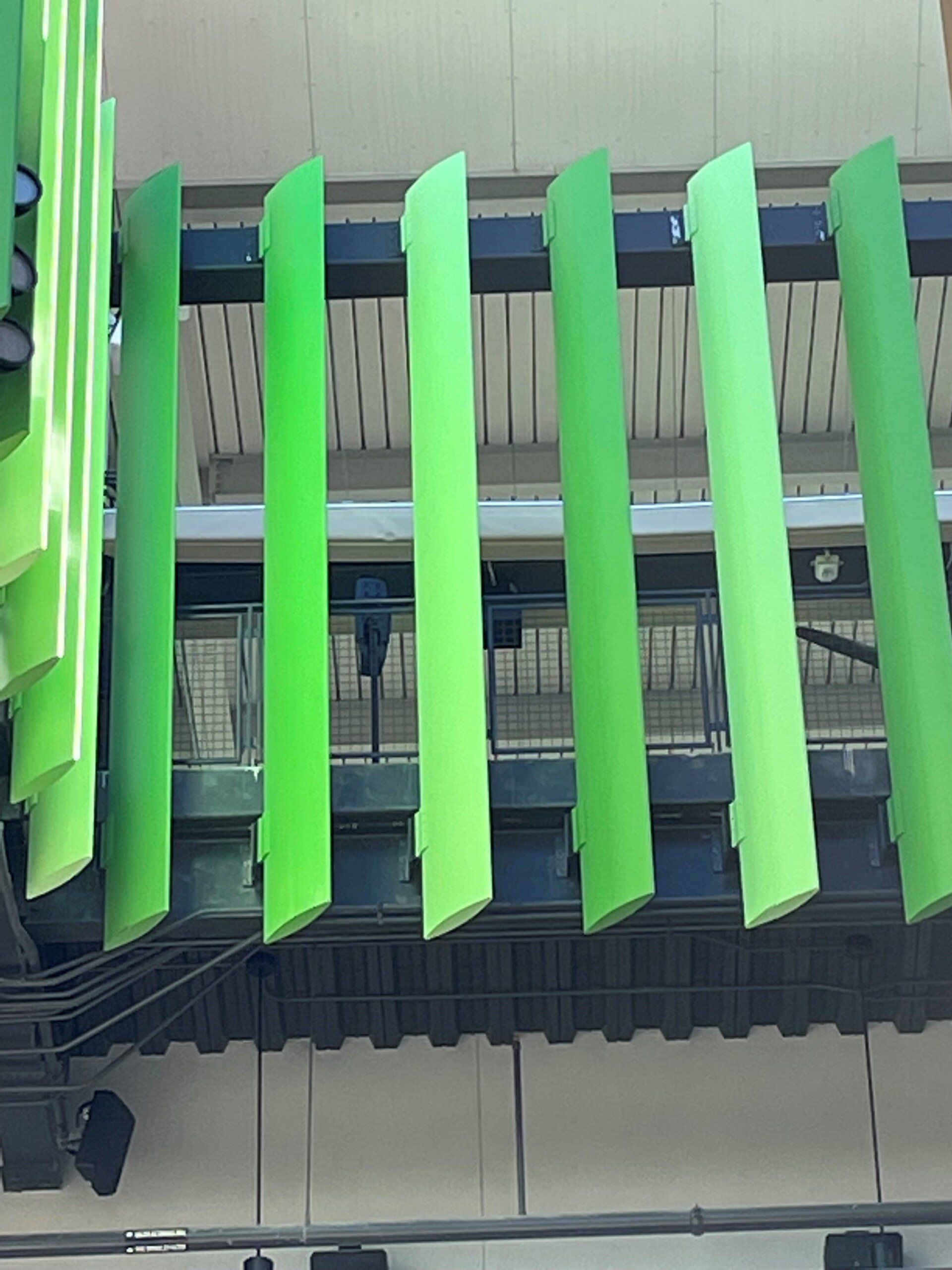 A row of green slats are hanging from the ceiling of a building.