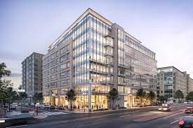 A large building with a lot of windows is on the corner of a city street.