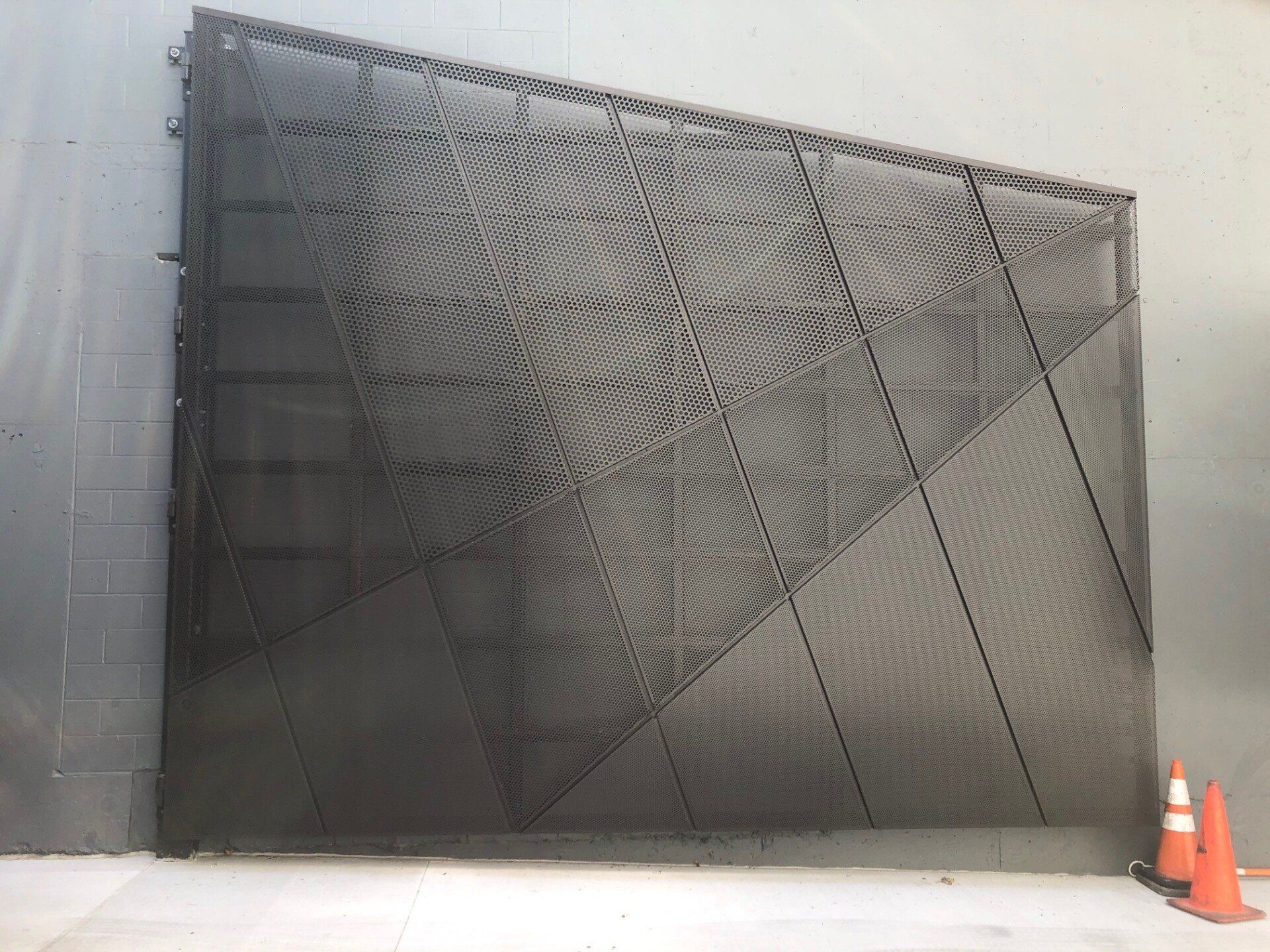 A gray wall with a geometric design and orange cones in front of it