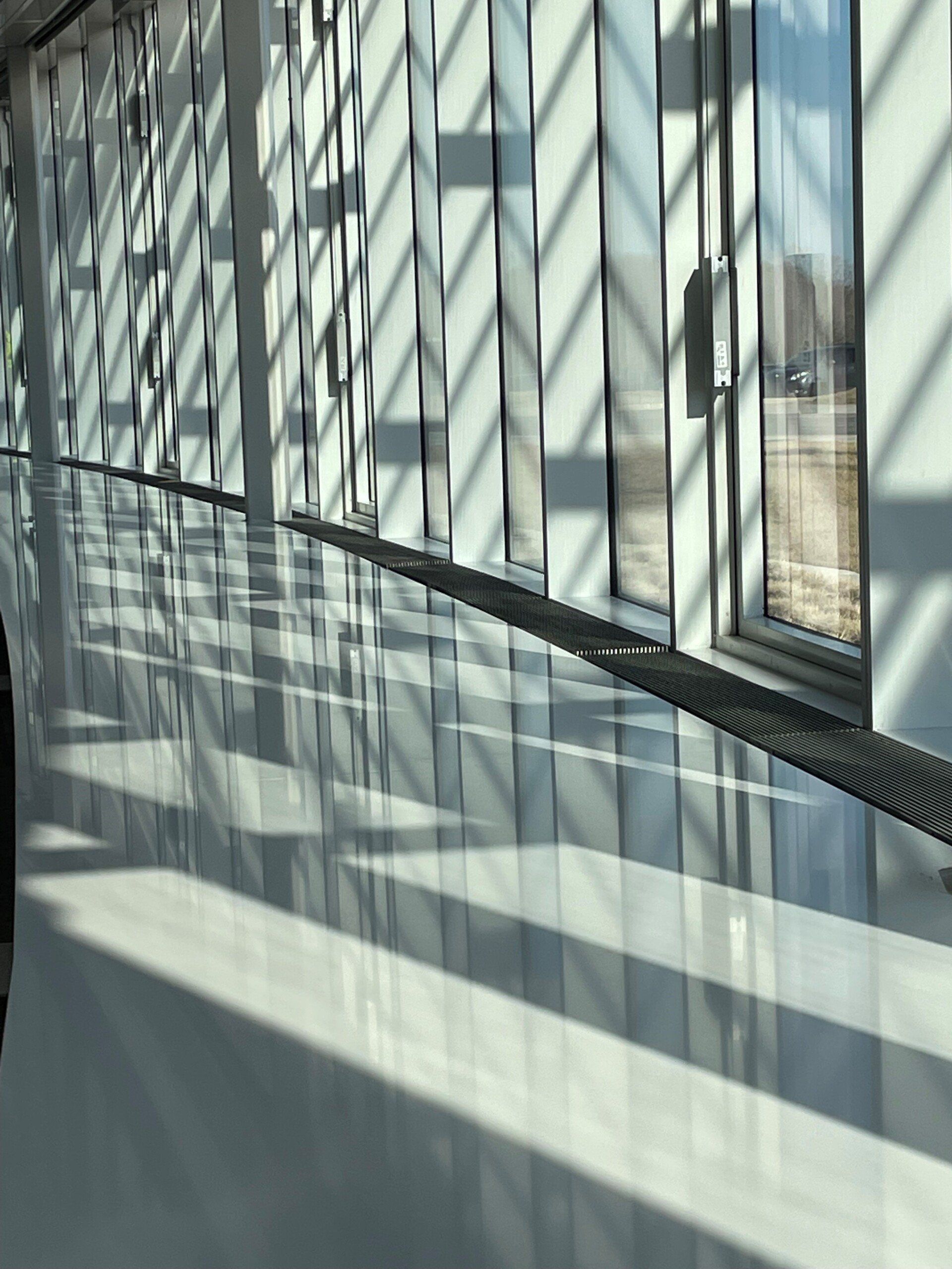 A long hallway with lots of windows and shadows on the floor
