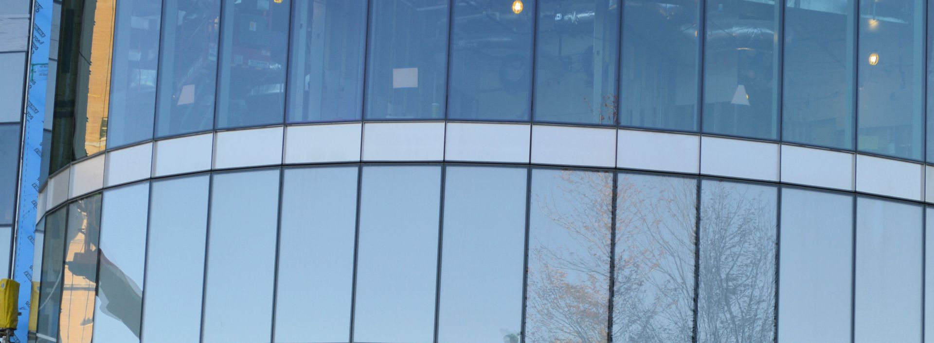 A large building with a lot of windows and a tree reflected in the windows.