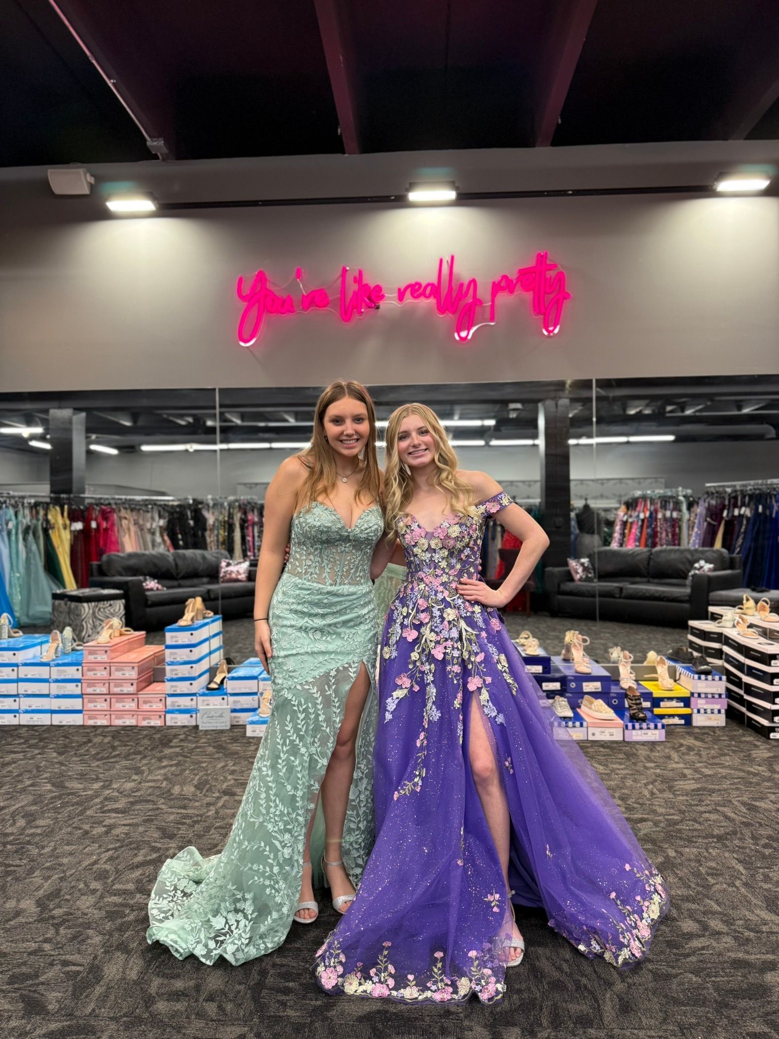 Woman in formal gown, seated on pink couch, under neon sign that says