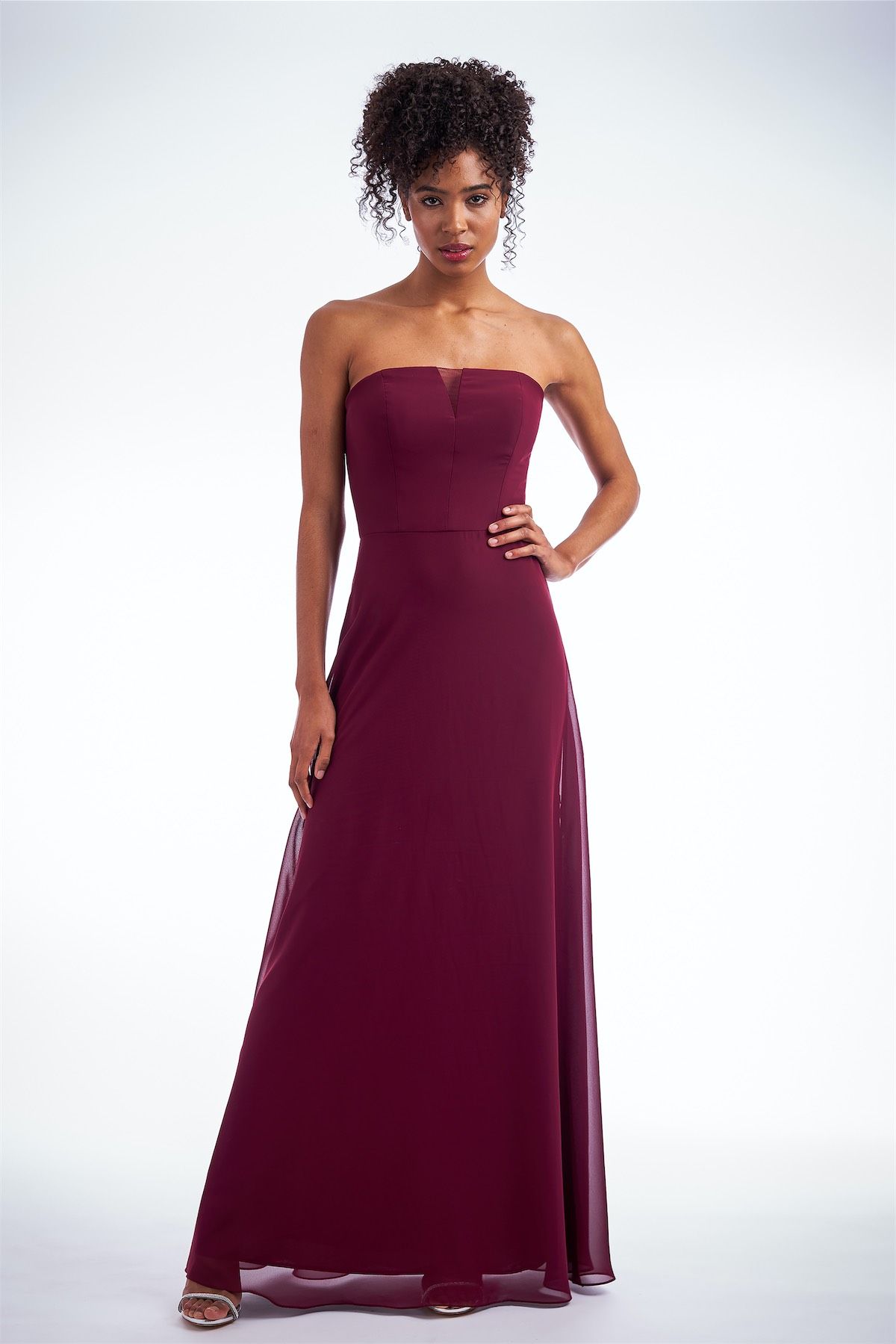 Woman in a strapless burgundy gown, standing with hand on hip. Studio shot.