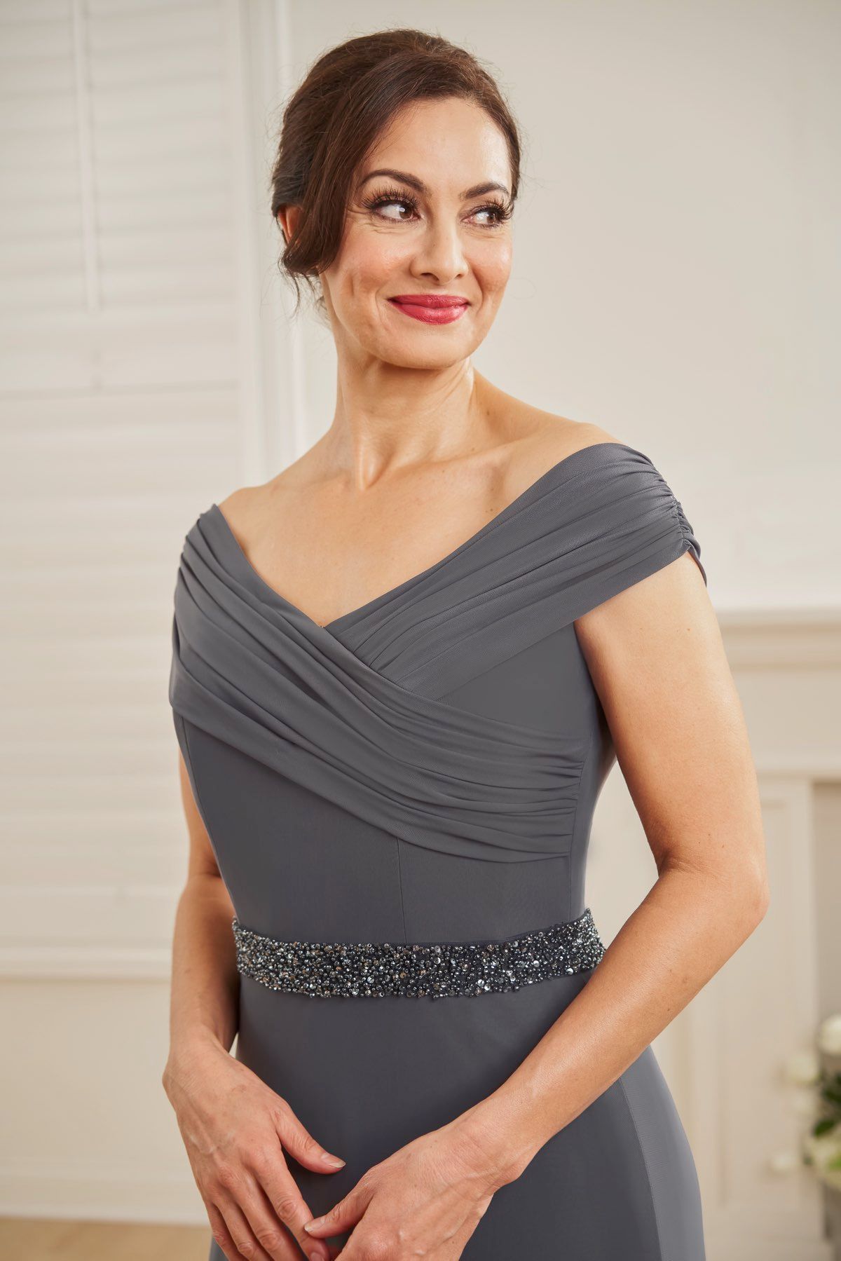 Woman in gray formal dress, looking off to the side, wearing a beaded belt, indoor setting.