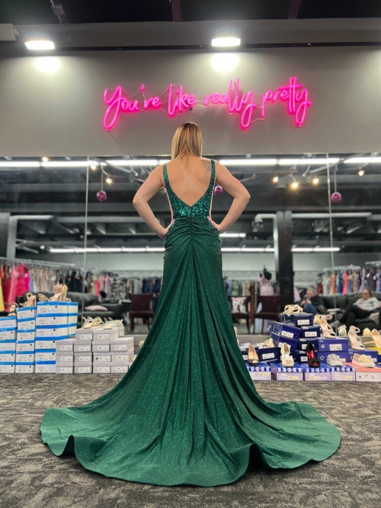 Woman in green sparkly gown, hands on hips, in a dress shop.