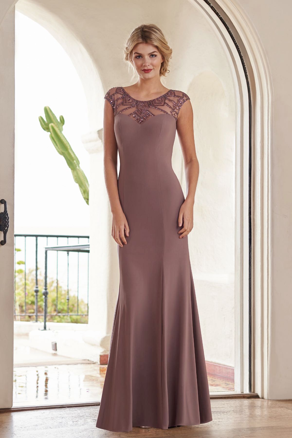 Woman in a mauve formal dress with beaded neckline stands in an arched doorway.
