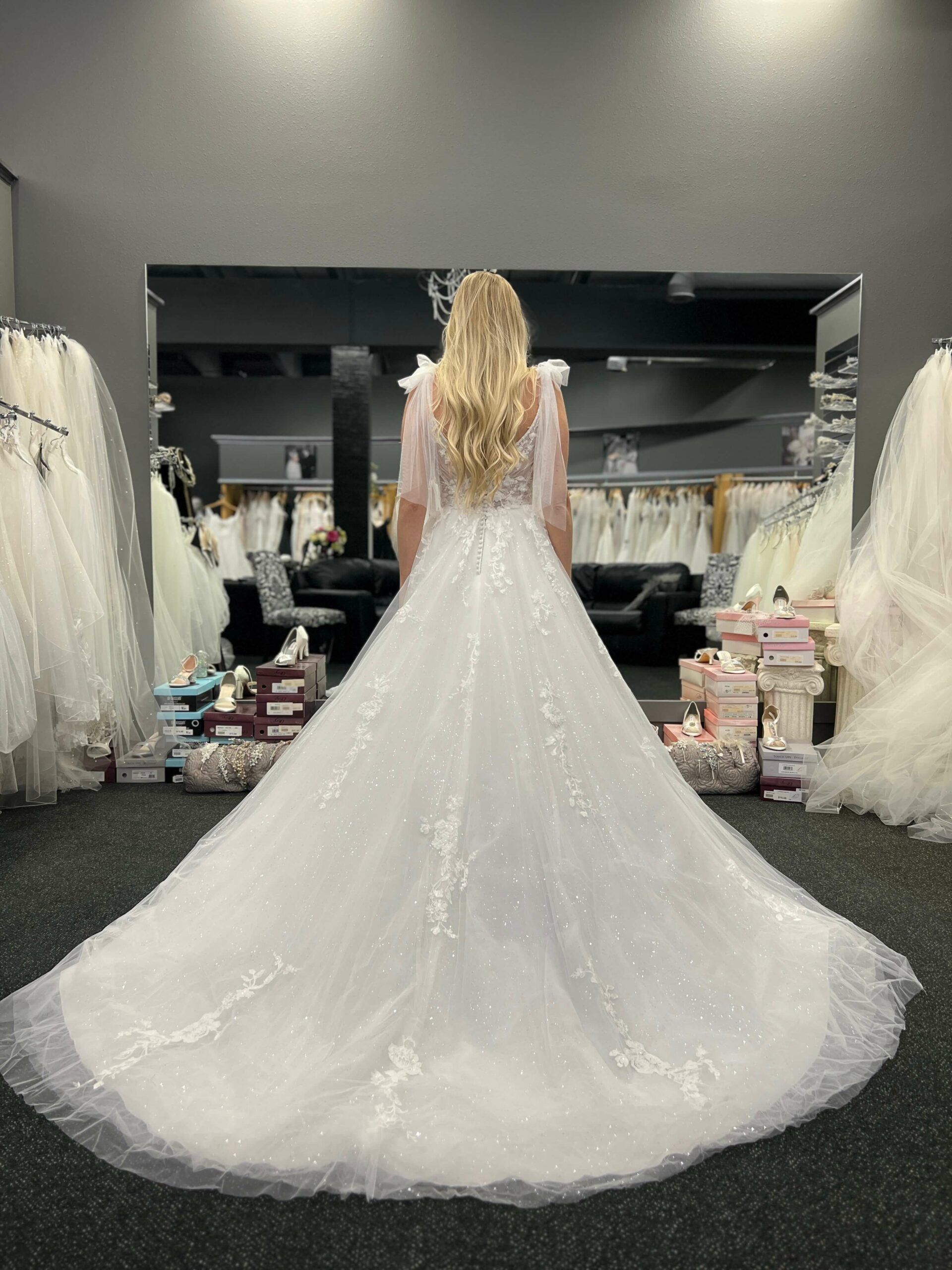 Woman in a white wedding gown with a long train, standing in a bridal shop.