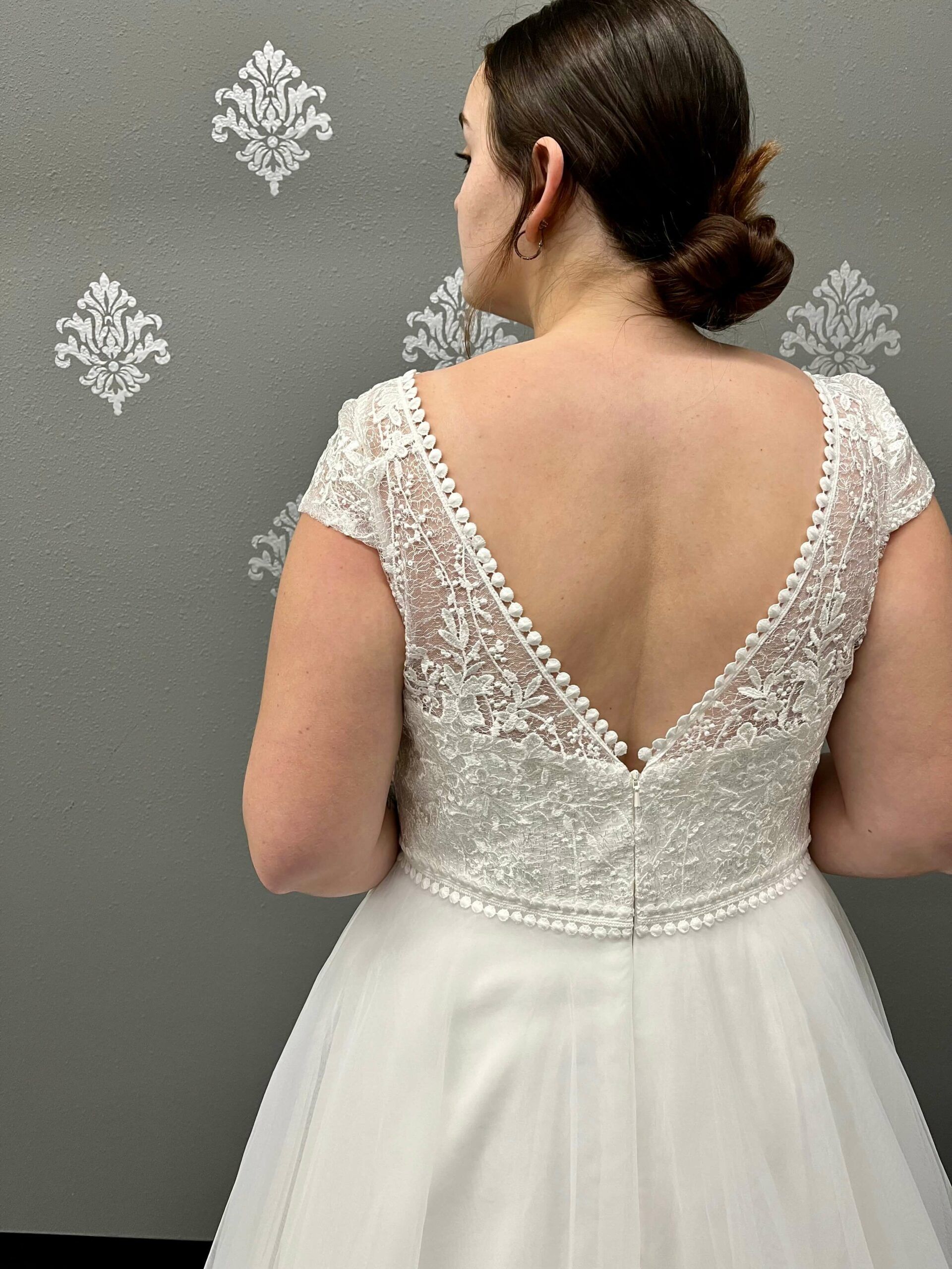 Woman in a white wedding dress, back view, low V-neck with lace detailing.