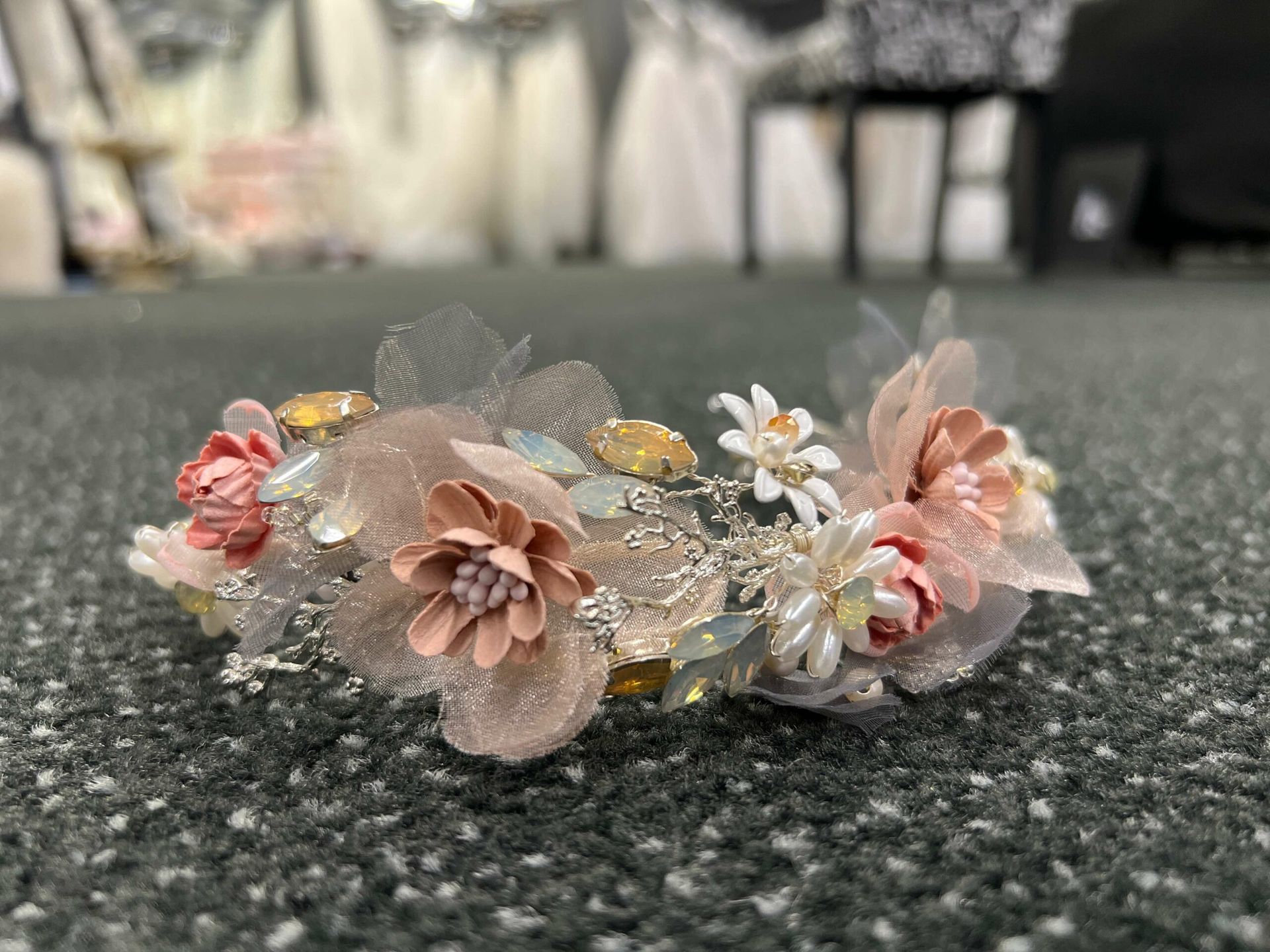 Floral hairpiece with pink, peach, and white flowers, silver accents, and tulle on gray carpet.